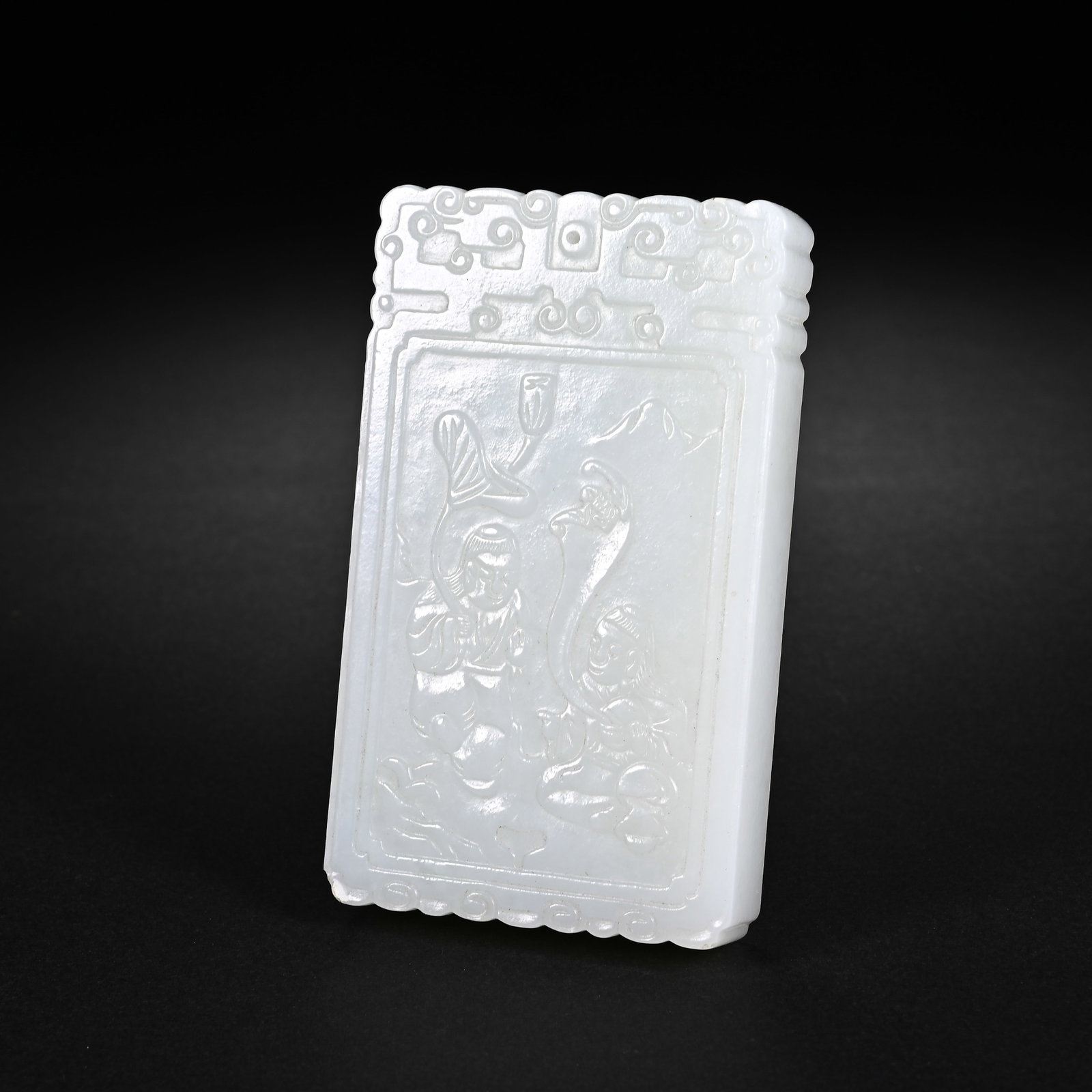 A CHINESE WHITE HETIAN JADE RECTANGULAR PLAQUE: A CHINESE WHITE HETIAN JADE RECTANGULAR PLAQUE This rectangular jade pendant is carved from smooth pale white Hetian nephrite, measuring 7.8cm tall, 4.6cm wide and 1.2cm thick. The top edge is decorat