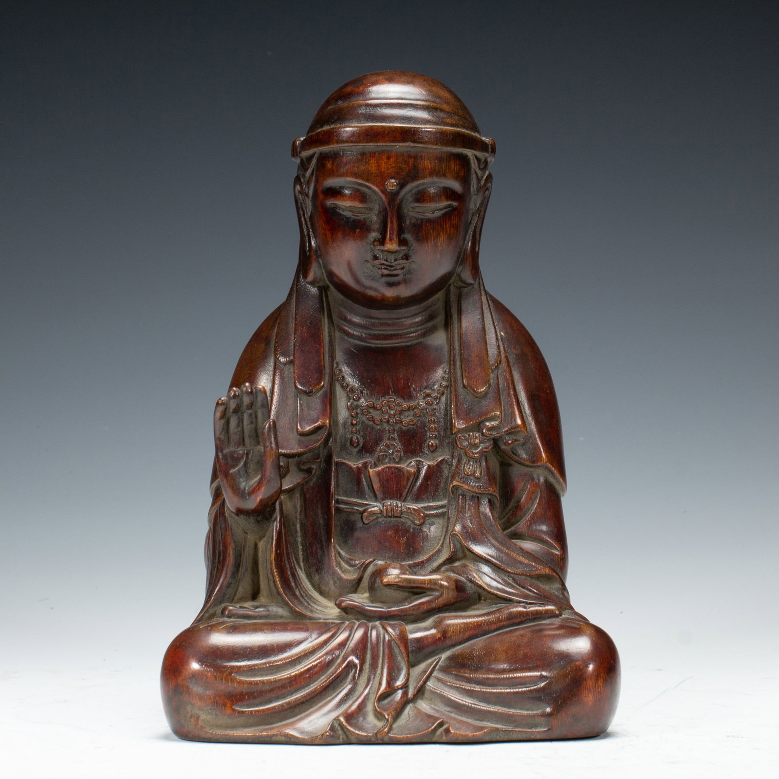 A CHINESE AGARWOOD SEATED DEITY FIGURE: A CHINESE AGARWOOD SEATED DEITY FIGURE A serene seated deity figure masterfully carved from natural agarwood with rich deep reddish-brown patina and distinct natural wood grain. The figure sits in ful