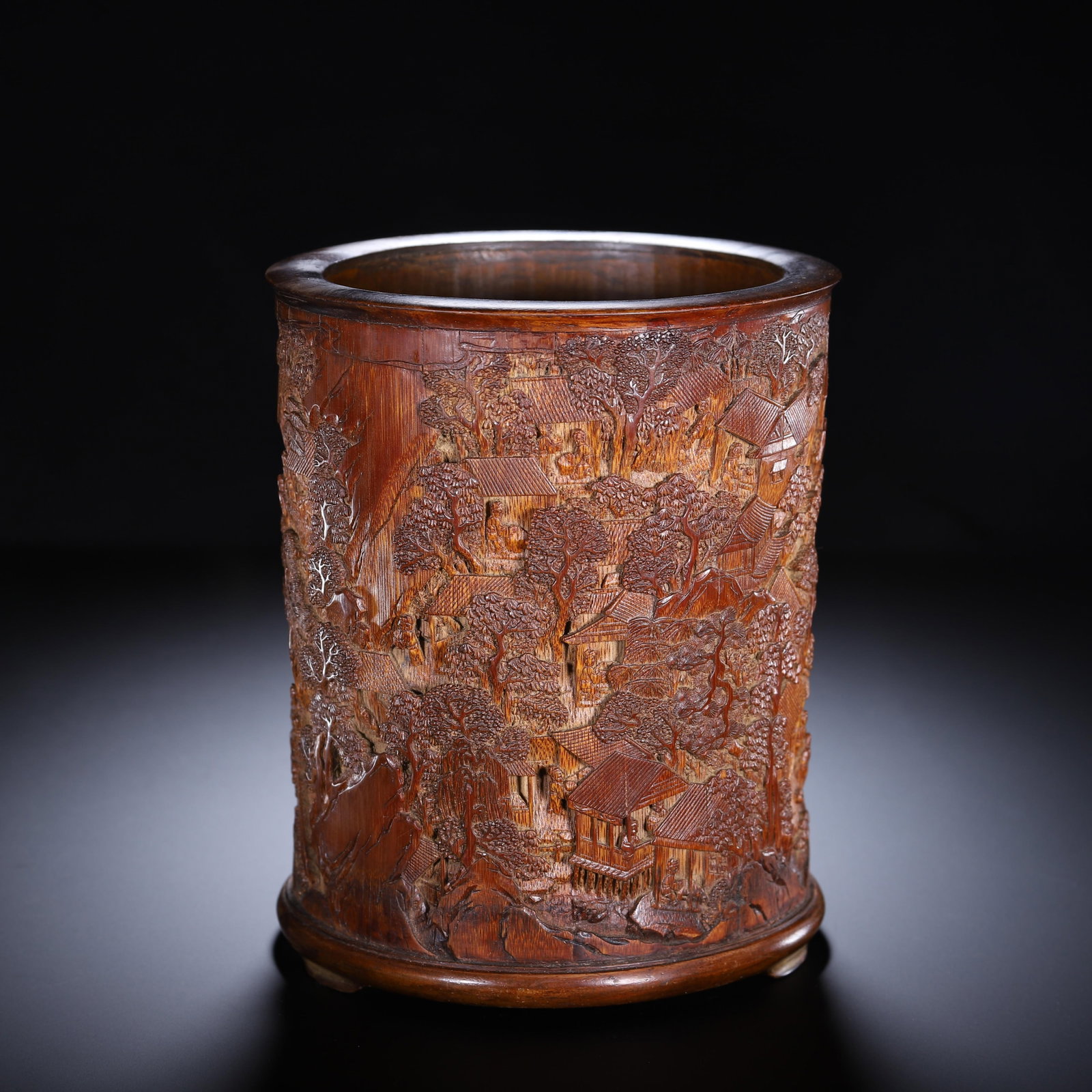 A CHINESE CARVED BAMBOO LANDSCAPE BRUSH POT: A CHINESE CARVED BAMBOO LANDSCAPE BRUSH POT A cylindrical brush pot meticulously carved from aged bamboo with rich warm amber patina and natural grain texture. The entire outer wall is rendered in dee