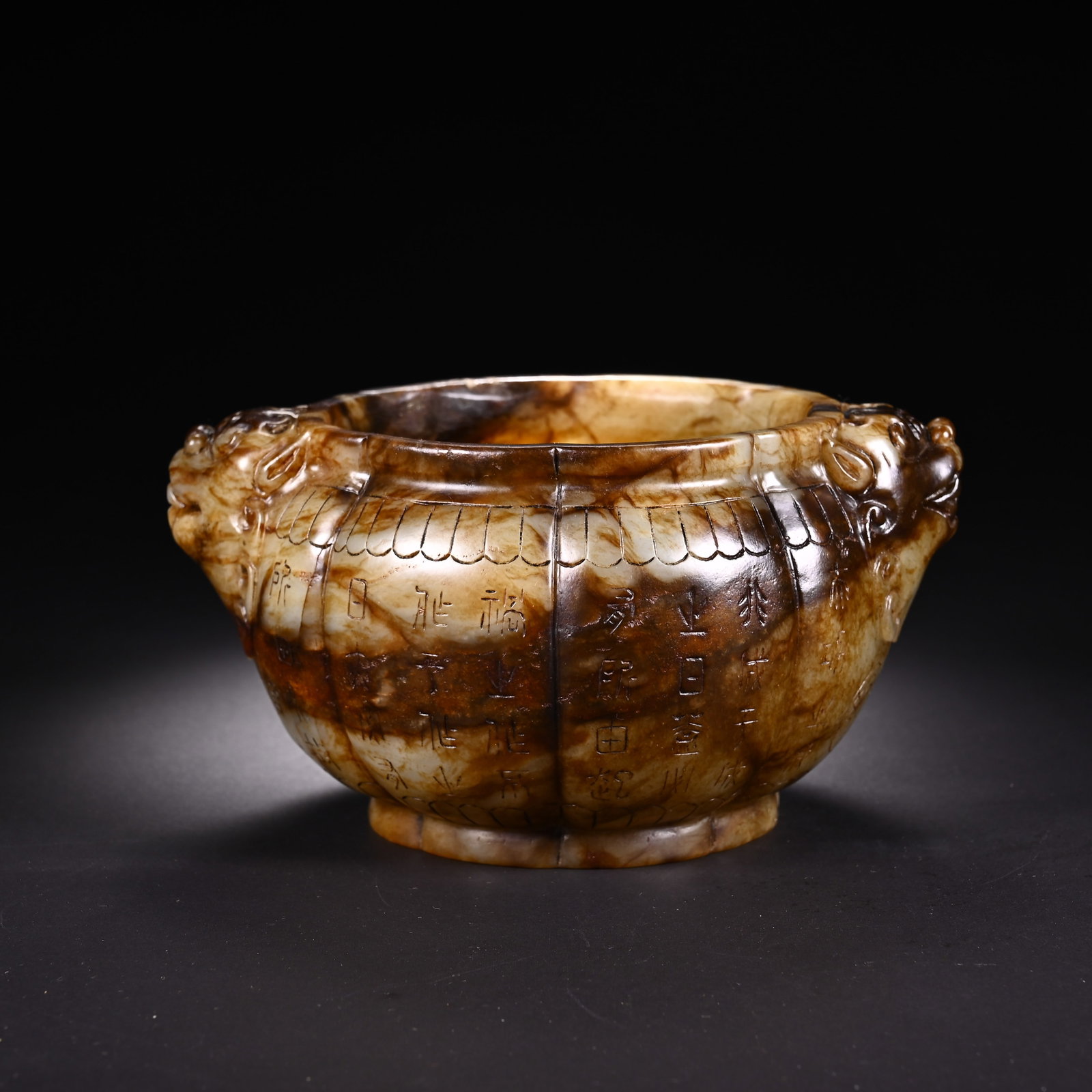 A CHINESE INSCRIBED JADE BOWL WITH TWIN MYTHICAL BEAST HANDLES: A CHINESE INSCRIBED JADE BOWL WITH TWIN MYTHICAL BEAST HANDLES This lobed jade bowl is fitted with two finely sculpted beast head handles on its flared rim. The stone displays rich interwoven pale cre