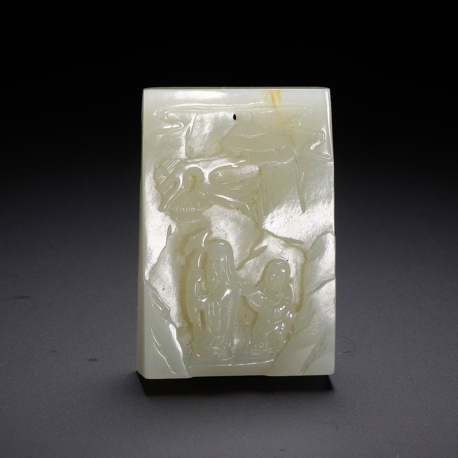 A CHINESE HETIAN JADE FIGURAL PENDANT PLAQUE: A CHINESE HETIAN JADE FIGURAL PENDANT PLAQUE A rectangular wearable plaque carved from smooth pale Hetian nephrite jade with faint natural russet streaks at the top edge. The front face is rendered in