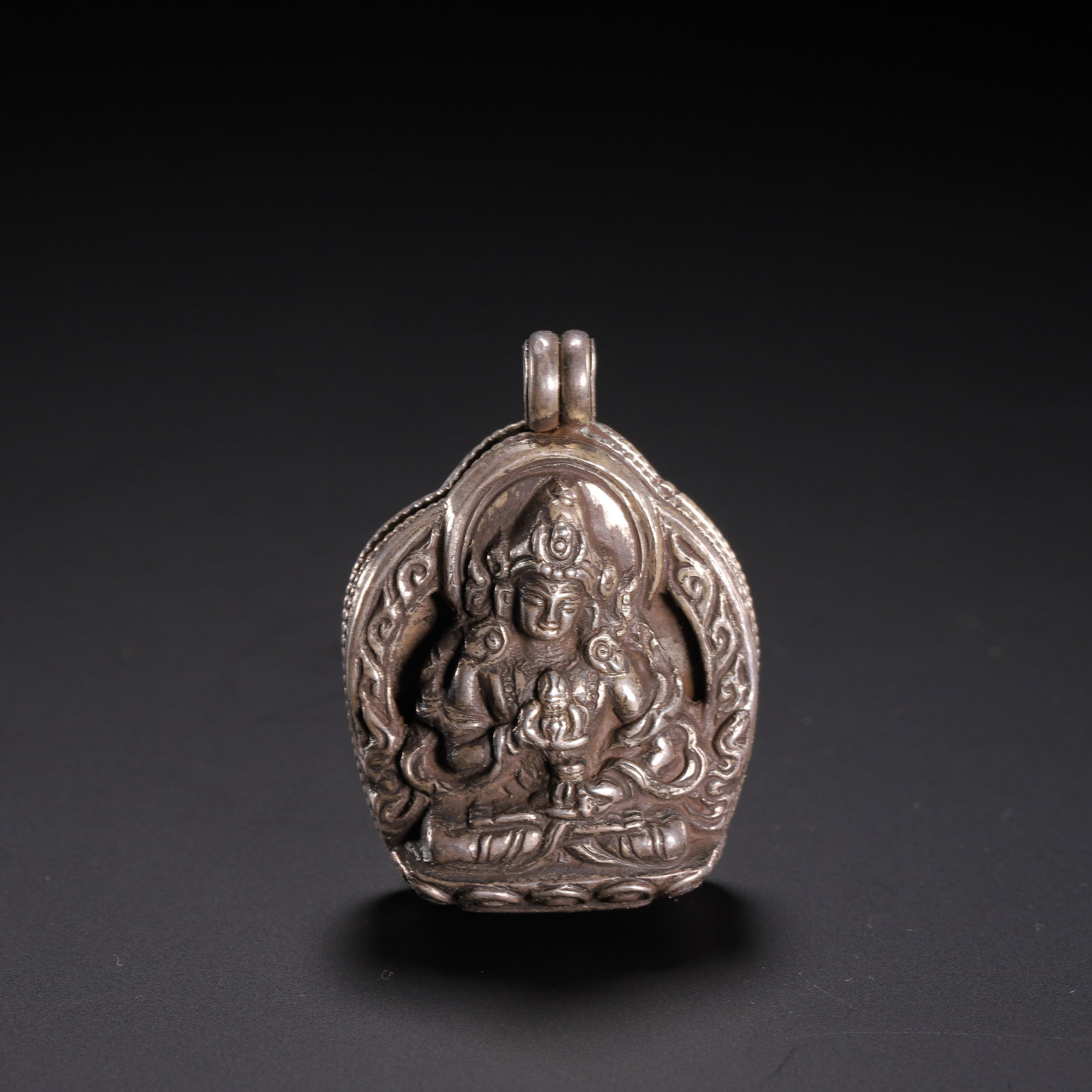 A CHINESE TIBETAN SILVER GAU AMULET BOX: A CHINESE TIBETAN SILVER GAU AMULET BOX This portable devotional gau pendant is crafted from solid silver, shaped into a curved arched locket form with dual suspension loops at the apex for cord wear.