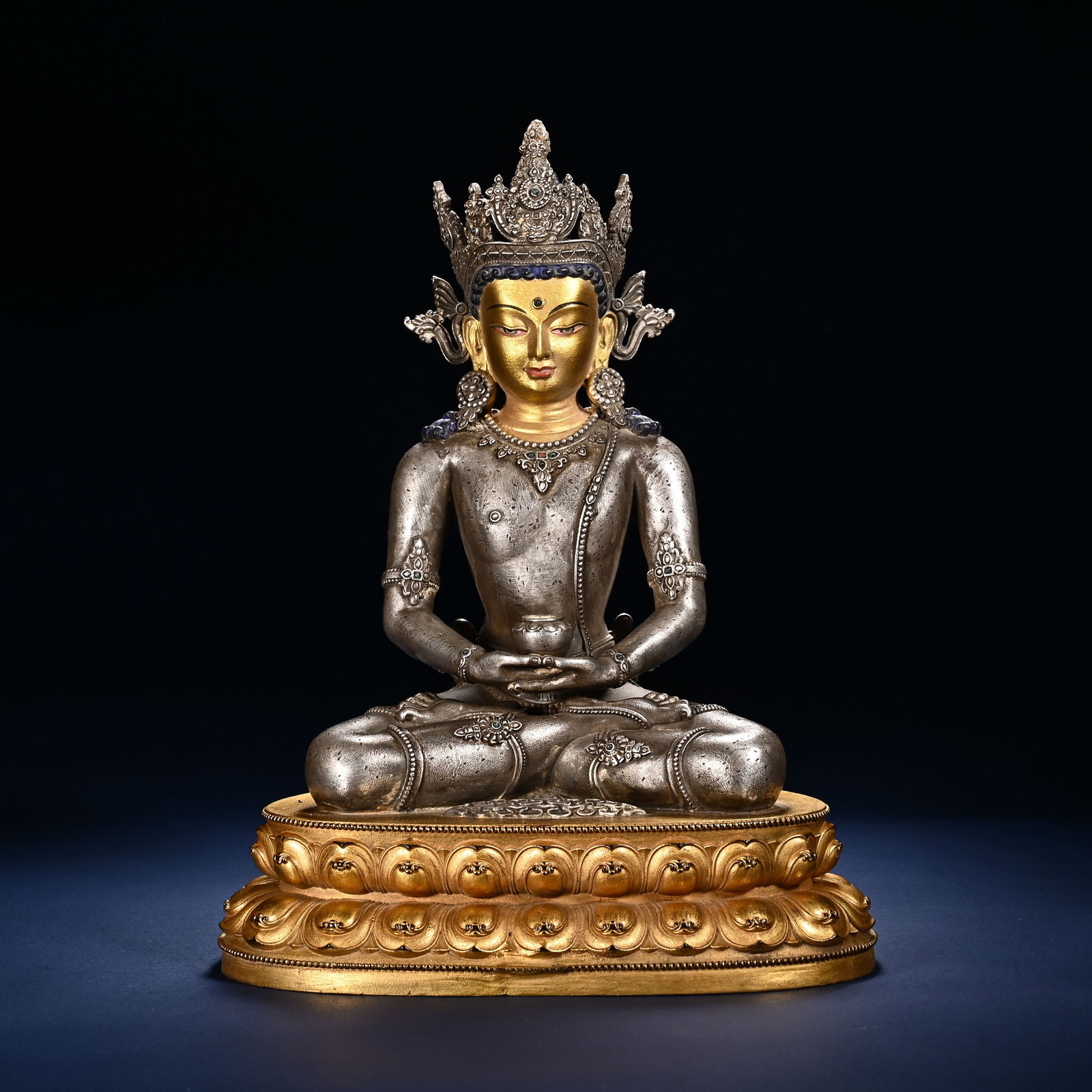 A CHINESE PARTIALLY GILT SILVERED COPPER BUDDHA: A CHINESE PARTIALLY GILT SILVERED COPPER BUDDHA This seated Buddhist deity statue is cast in copper with silvered torso and limbs, contrasted by fully gilded face and double lotus pedestal. The figure