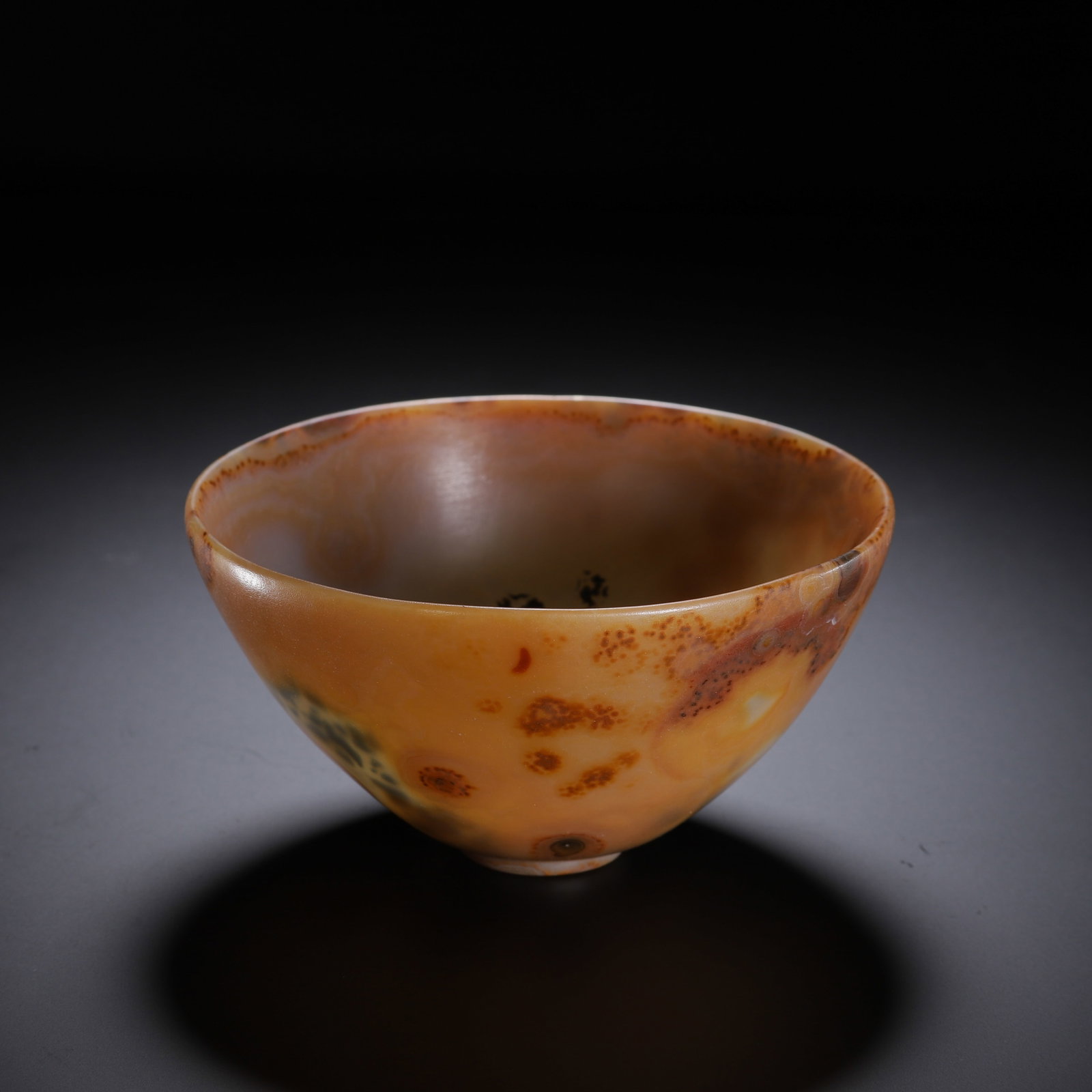 A CHINESE NATURAL PATTERN AGATE BOWL: A CHINESE NATURAL PATTERN AGATE BOWL This elegant tapered bowl is entirely hollowed and polished from a single piece of natural agate. The stone boasts a warm honey-amber base naturally streaked with 