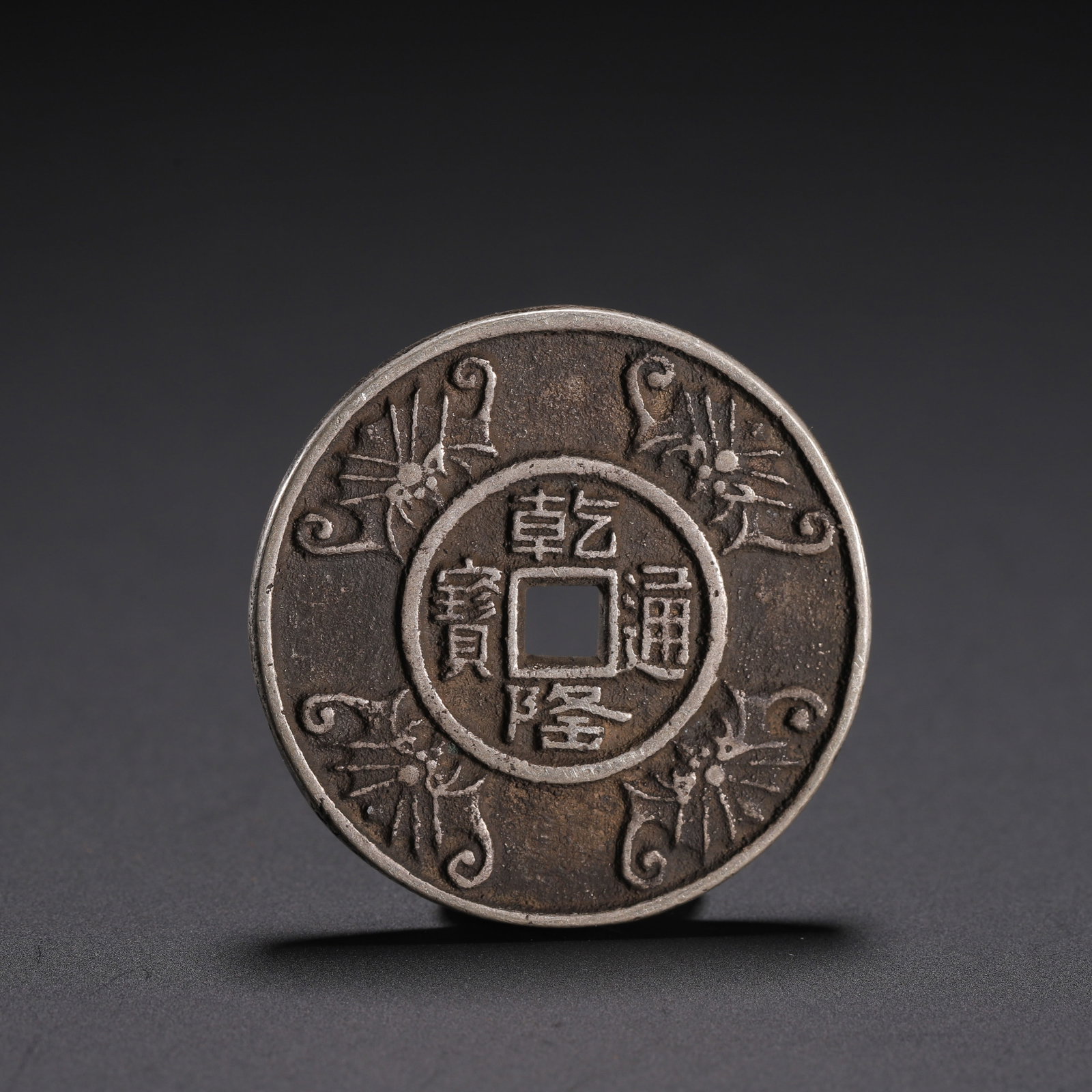 A CHINESE SILVER QIANLONG CHARM COIN: A CHINESE SILVER QIANLONG CHARM COIN This circular silver charm features a central square aperture, inscribed with four regular script characters ?Qianlong Tongbao? within a double circular border. Fo