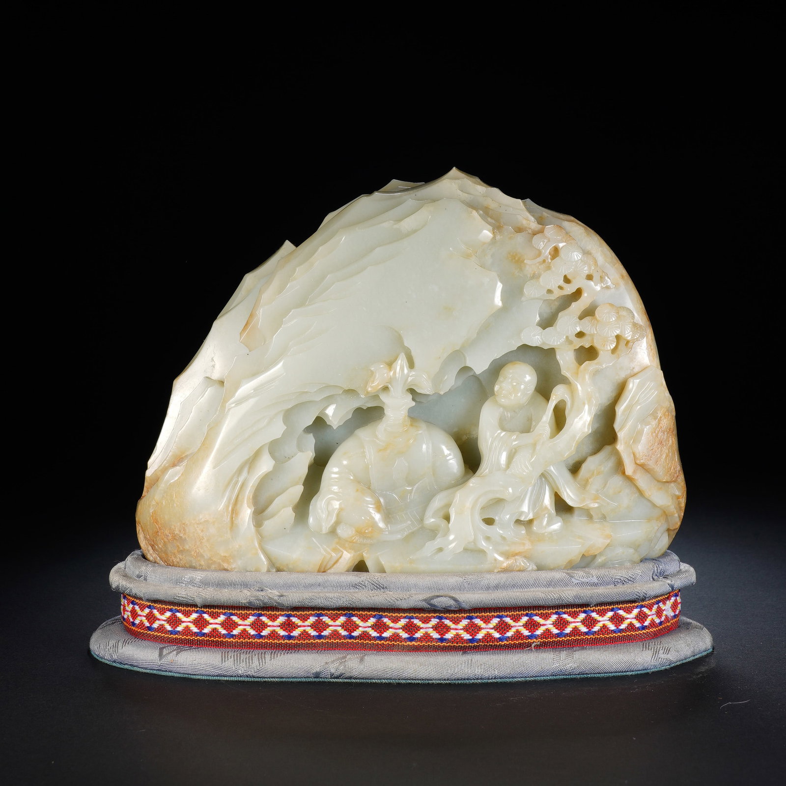 A CHINESE WHITE JADE MOUNTAIN BOULDER WITH FIGURAL SCENE: A CHINESE WHITE JADE MOUNTAIN BOULDER WITH FIGURAL SCENE This nephrite jade mountain carving measures 18cm ? 6cm ? 13cm, with a total height of 16cm on its fabric-wrapped stand, weighing 2394 grams. R