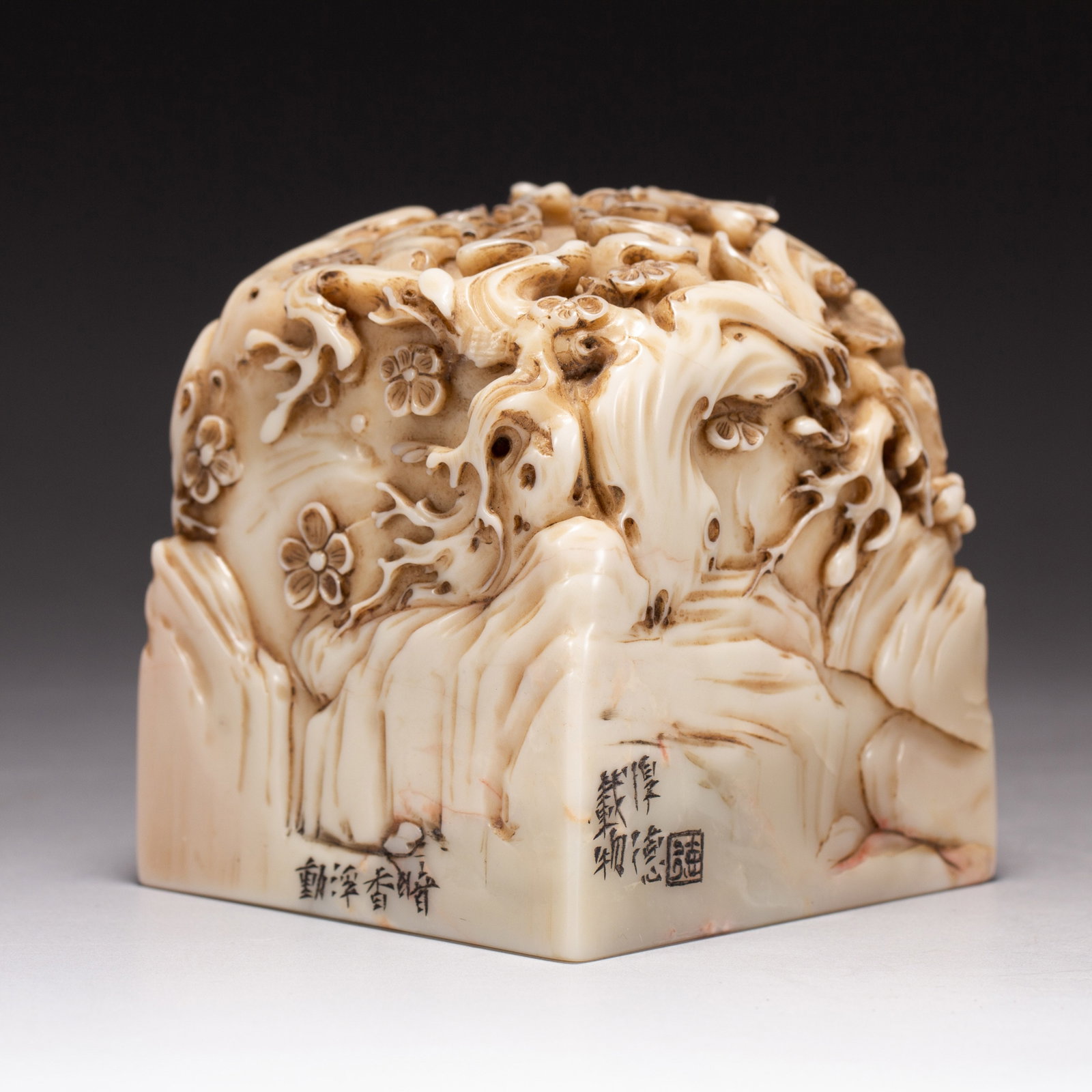 A CHINESE SHOUSHAN STONE SQUARE SEAL WITH FLORAL CARVED FINIAL: A CHINESE SHOUSHAN STONE SQUARE SEAL WITH FLORAL CARVED FINIAL This substantial square seal is hewn from creamy pale Shoushan soapstone marked with subtle russet veining and natural mottling. Its dome