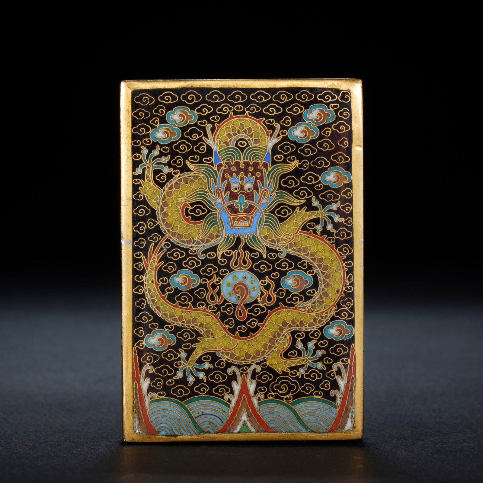 A CHINESE CLOISONNE DRAGON PAPER WEIGHT: A CHINESE CLOISONNE DRAGON PAPER WEIGHT This rectangular cloisonne scholar's paper weight measures 4 cm wide, 6 cm tall and 1.5 cm thick, weighing 275 grams. It is crafted on gilt copper with a deep b