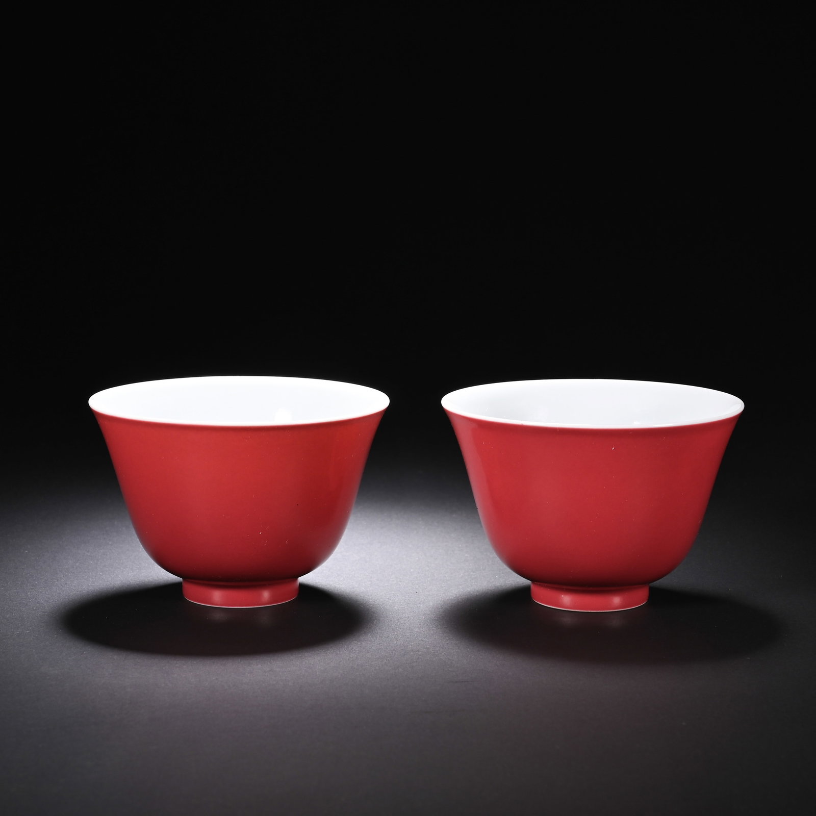 A PAIR OF CHINESE CARMINE GLAZED PORCELAIN CUPS: A PAIR OF CHINESE CARMINE GLAZED PORCELAIN CUPS This matched pair of wine cups features a classic tapering bell-shaped form with a small raised circular foot and wide flared rim. The exterior is entir