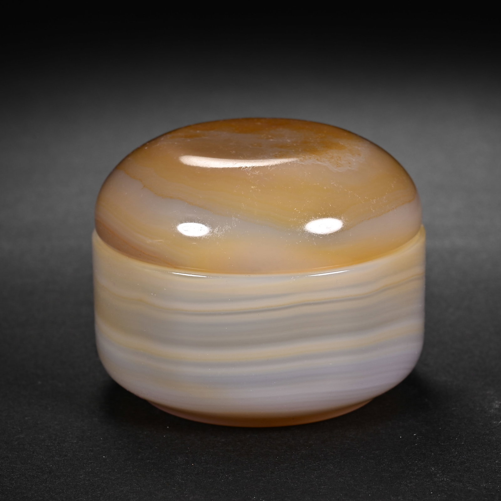 A CHINESE BANDED AGATE LIDDED COSMETIC BOX: A CHINESE BANDED AGATE LIDDED COSMETIC BOX This compact covered box is fully carved from natural banded agate featuring soft parallel strata of creamy white, pale beige and warm amber hues, polished t
