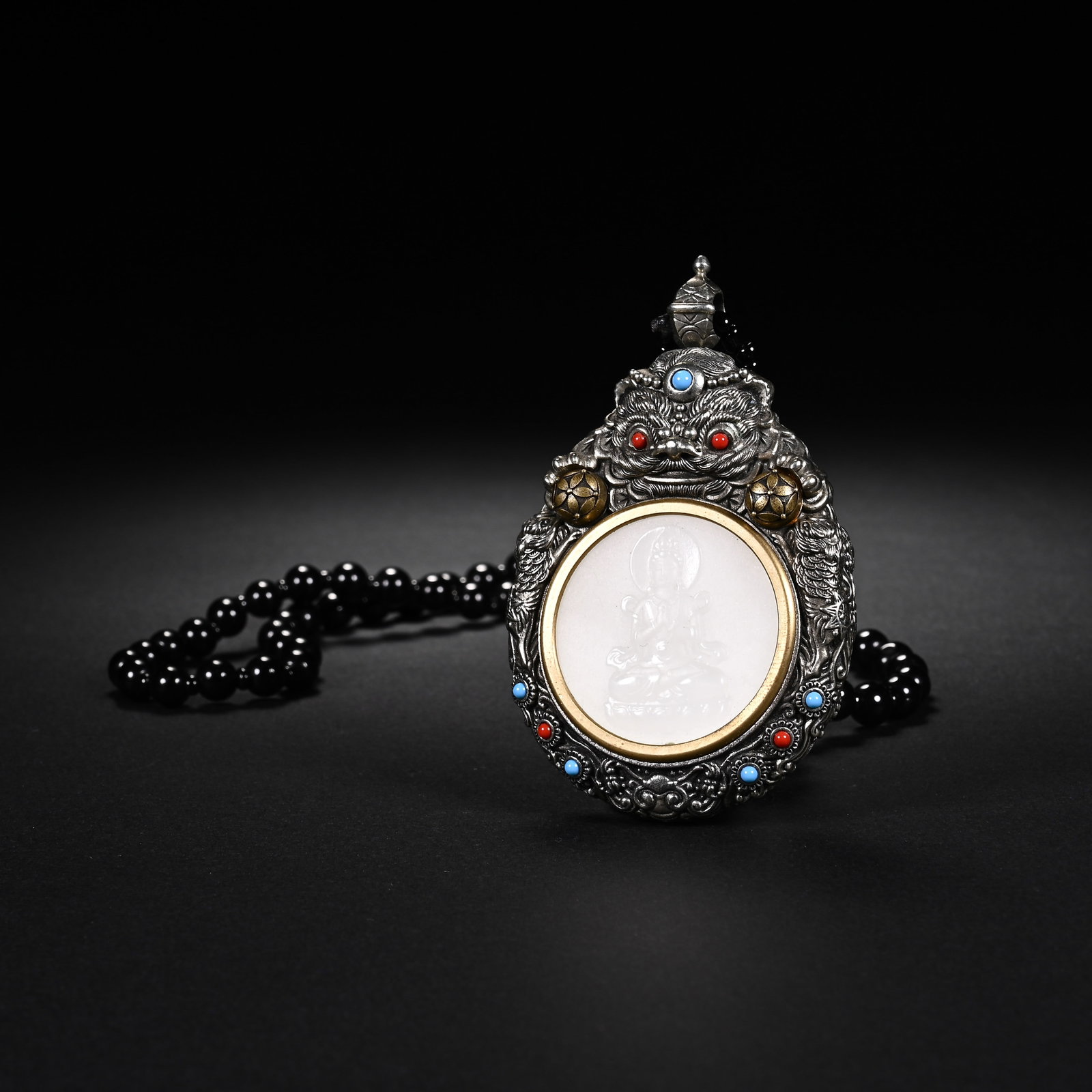 A CHINESE STERLING SILVER MOUNTED WHITE JADE PENDANT: A CHINESE STERLING SILVER MOUNTED WHITE JADE PENDANT This elaborate wearable ornament measures 7.3cm tall, 5cm wide and 1.6cm thick, set with a polished white jade disc finely carved with a seated Bud