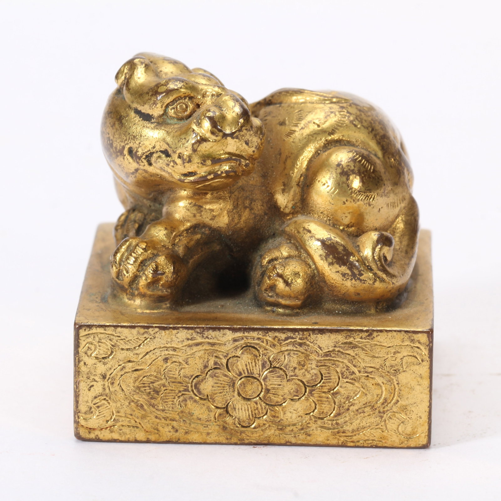 A CHINESE GILT BRONZE RECUMBENT MYTHICAL BEAST SEAL: A CHINESE GILT BRONZE RECUMBENT MYTHICAL BEAST SEAL This square bronze seal is entirely covered in aged gilding with scattered dark patina and wear revealing the base metal beneath. The finial takes t