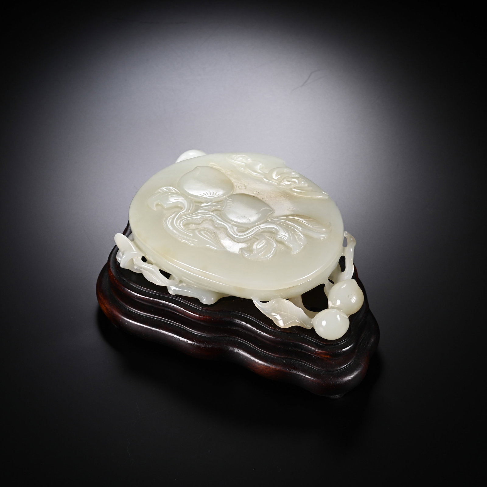 A CHINESE WHITE HETIAN JADE PEACH ORNAMENT: A CHINESE WHITE HETIAN JADE PEACH ORNAMENT This ornamental plaque is carved from smooth pale milky white Hetian nephrite with faint natural warm russet inclusions across its polished oval face. The fr