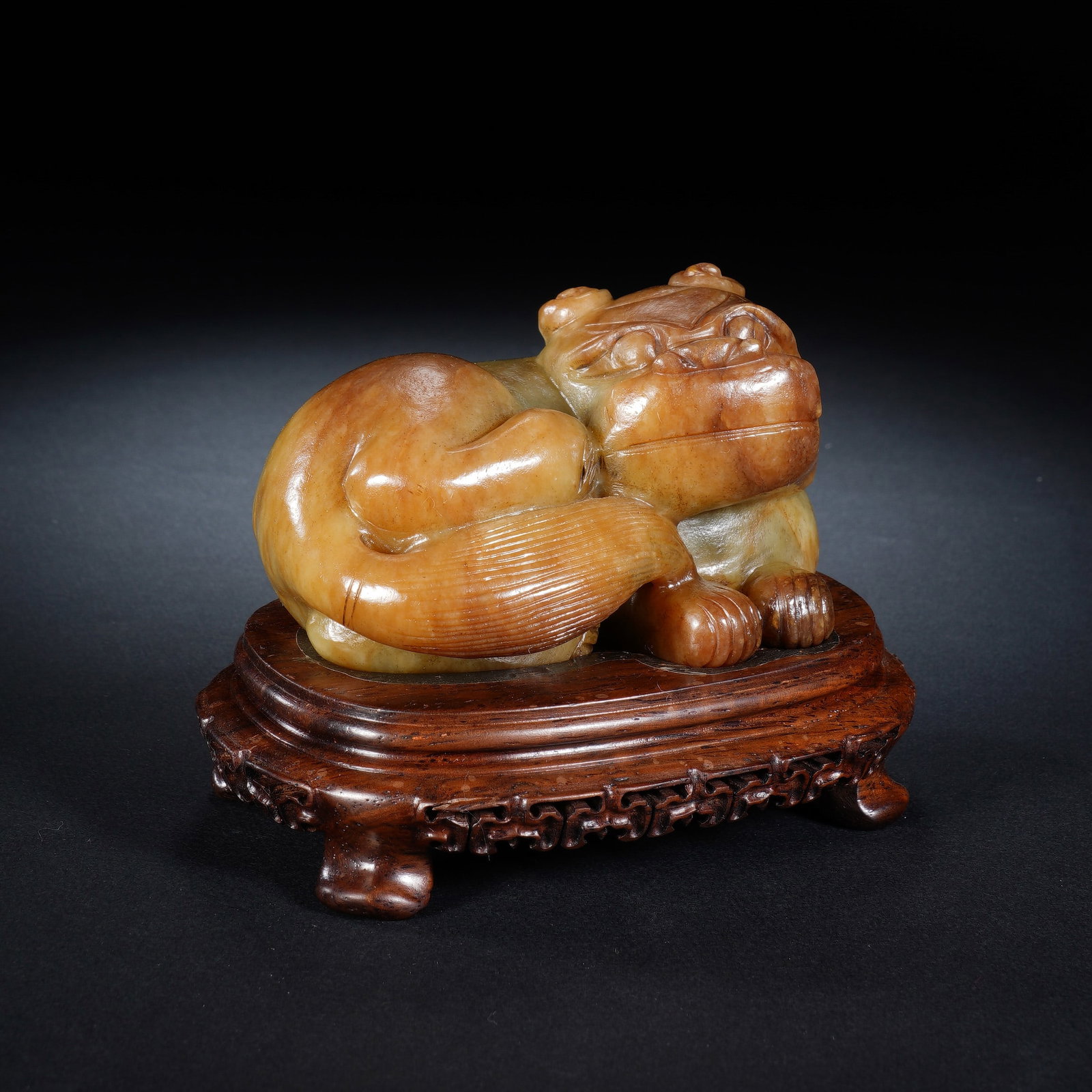 A CHINESE ANTIQUE JADE MYTHICAL BEAST WITH STAND: A CHINESE ANTIQUE JADE MYTHICAL BEAST WITH STAND The recumbent jade mythical beast measures 11 cm wide, 7.5 cm deep and 6 cm tall; the complete ensemble with carved hardwood stand is 12 cm wide, 8 cm 