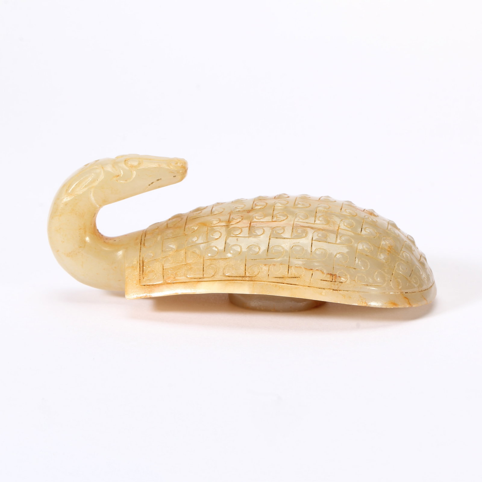 A CHINESE ARCHAIC JADE DRAGON BELT HOOK: A CHINESE ARCHAIC JADE DRAGON BELT HOOK This antique nephrite belt hook is carved from pale ivory jade suffused with natural russet skin streaks. The terminal is fashioned as a stylized dragon head wi