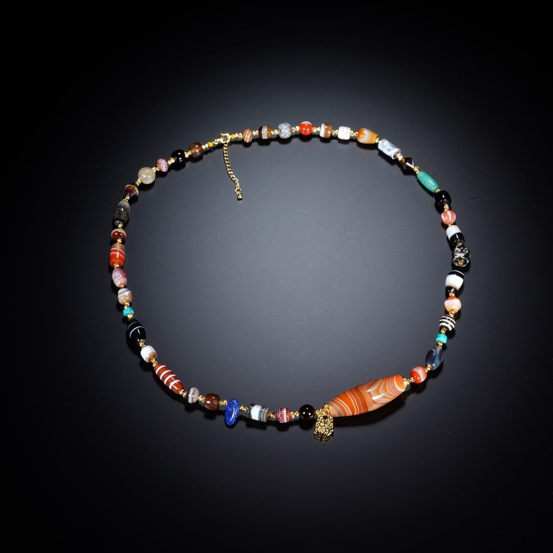 A CHINESE MULTI-STONE AGATE BEAD NECKLACE: A CHINESE MULTI-STONE AGATE BEAD NECKLACE This antique beaded necklace is strung with a diverse assemblage of hand-carved gemstone beads, centering on a large banded banded agate barrel pendant with n