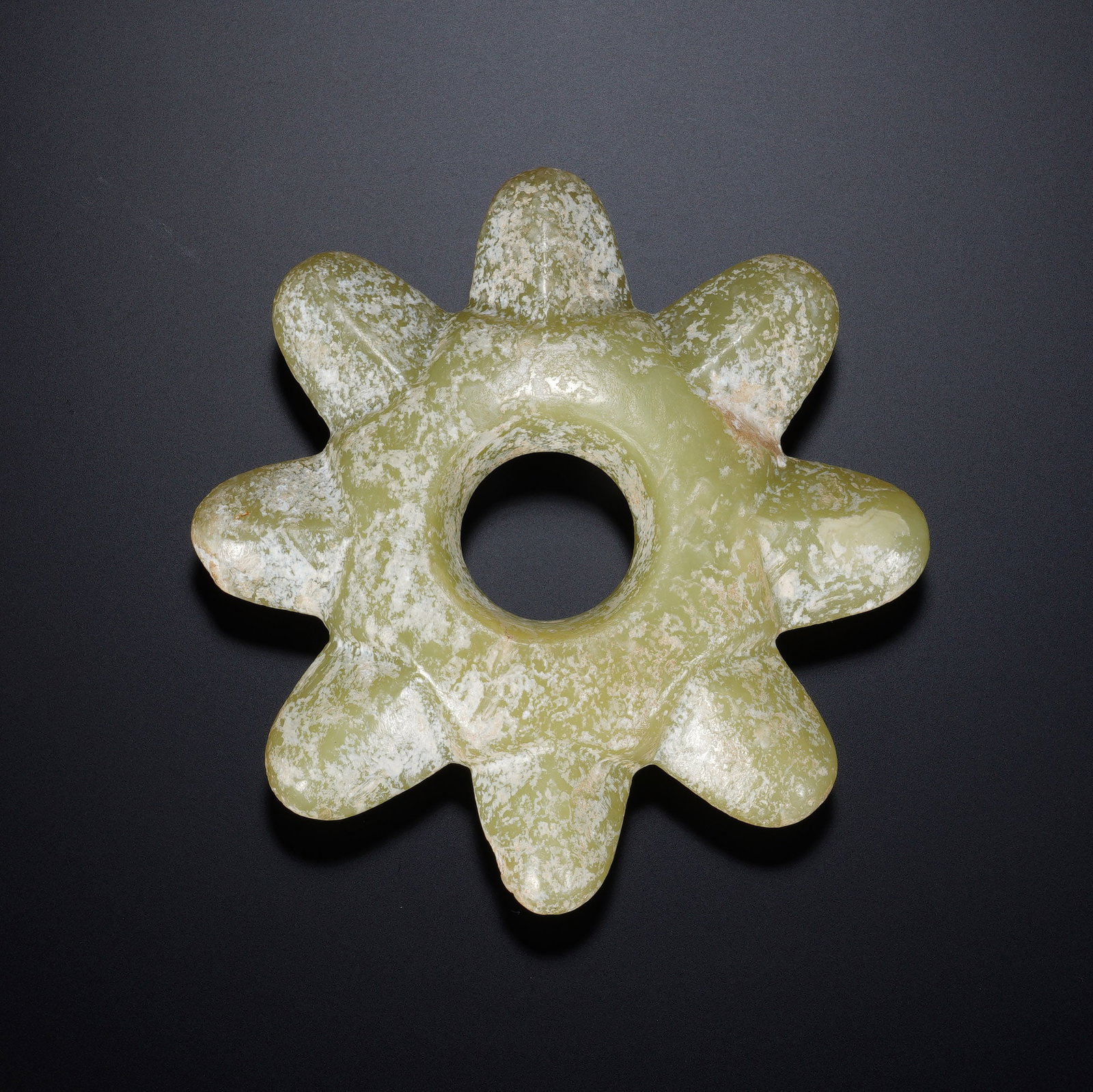 A CHINESE ARCHAIC MULTI-LOBED JADE PENDANT: A CHINESE ARCHAIC MULTI-LOBED JADE PENDANT This singular carved jade pendant measures 9.5 cm across with a thickness of 1.7 cm and weighs 140 grams. It features a central circular perforation surround