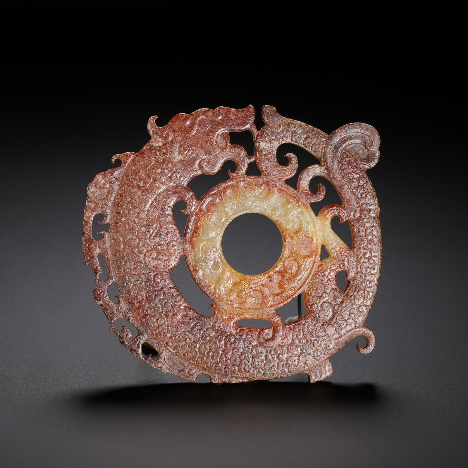 A CHINESE ARCHAIC OPENWORK DRAGON JADE BI DISC: A CHINESE ARCHAIC OPENWORK DRAGON JADE BI DISC This elaborate jade bi ornament features a central smooth annular disc encircled by a coiled openwork dragon in full relief. The entire surface is densel