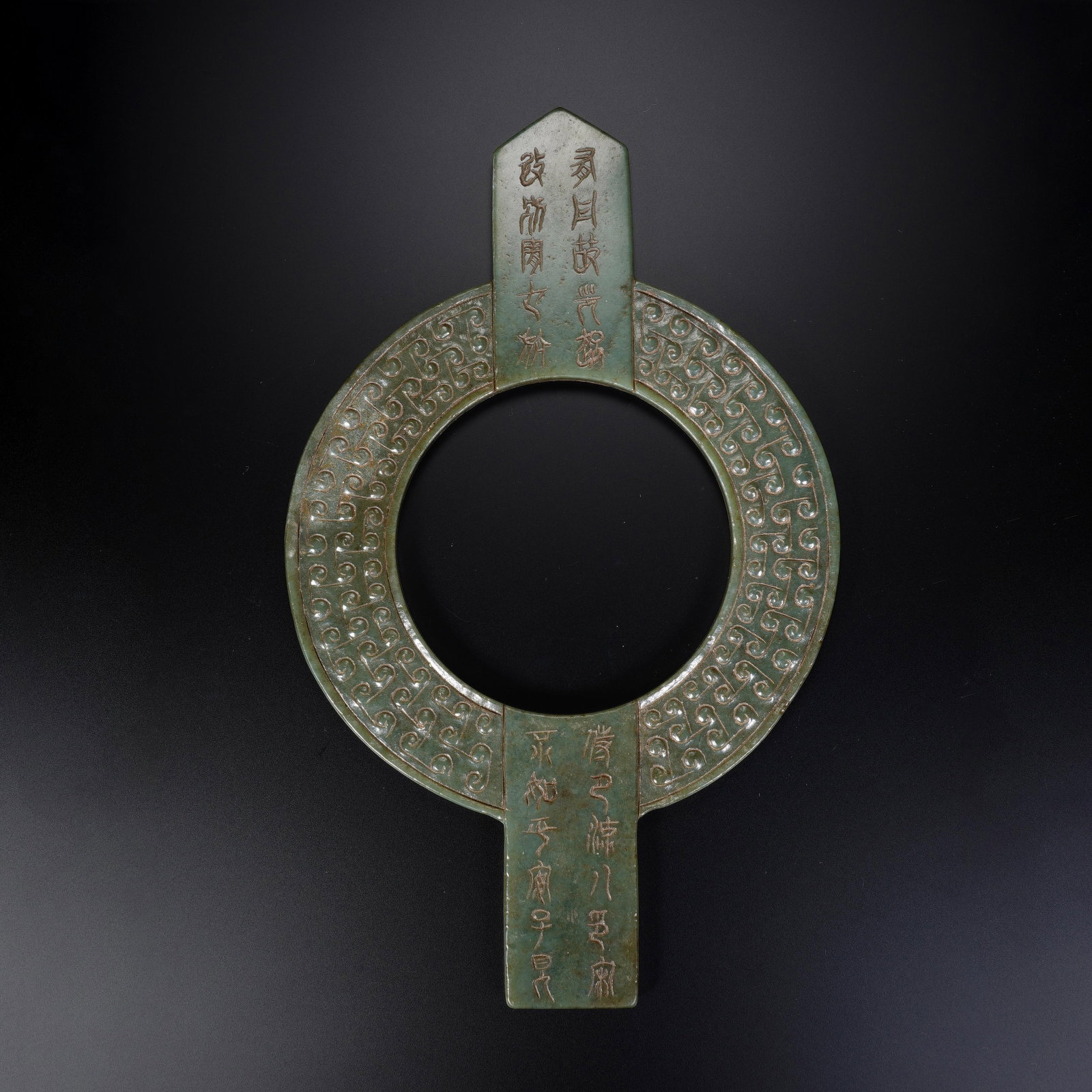 A CHINESE ARCHAIC INSCRIBED JADE BI: A CHINESE ARCHAIC INSCRIBED JADE BI This composite jade bi ornament measures 14.5 cm wide across the circular ring, 23 cm in full vertical length and 0.8 cm thick, weighing 294 grams. The annular disc