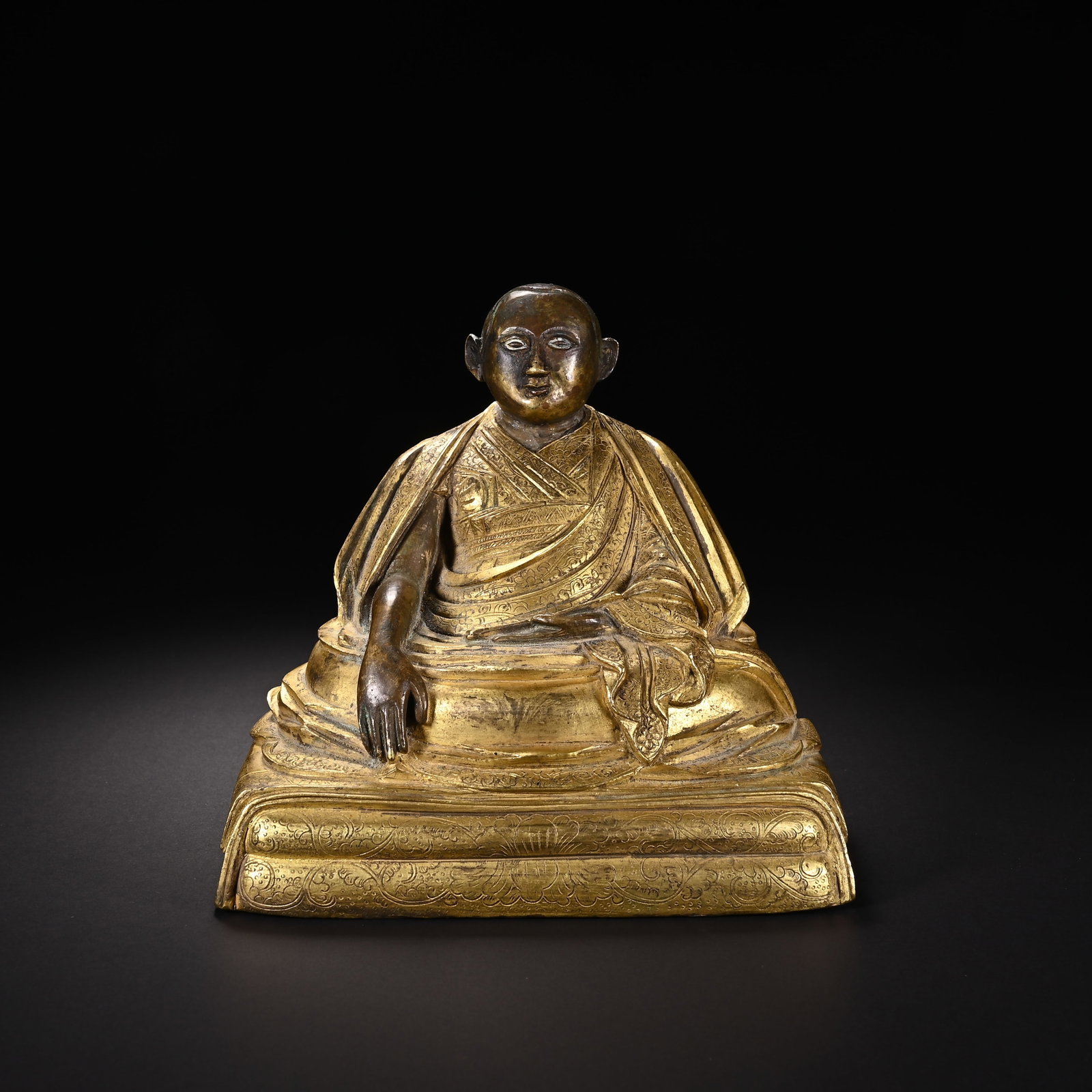 A CHINESE GILT BRONZE SEATED LAMA FIGURE: A CHINESE GILT BRONZE SEATED LAMA FIGURE This devotional sculpture is cast in copper alloy with partial gilding, portraying a Tibetan lama seated in relaxed meditation upon a layered rectangular lotus