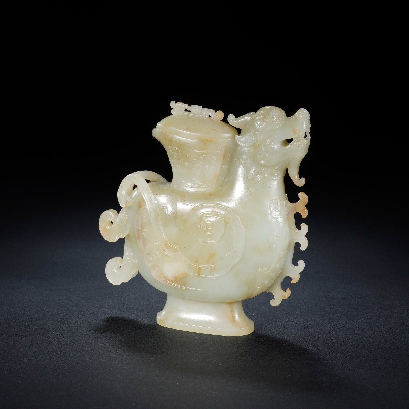 A CHINESE WHITE JADE DRAGON FORM EWER: A CHINESE WHITE JADE DRAGON FORM EWER This mythical beast-shaped jade ewer measures 11 cm wide, 2.5 cm deep and 12 cm tall, weighing 378 grams. Carved from pale celadon nephrite naturally streaked wit