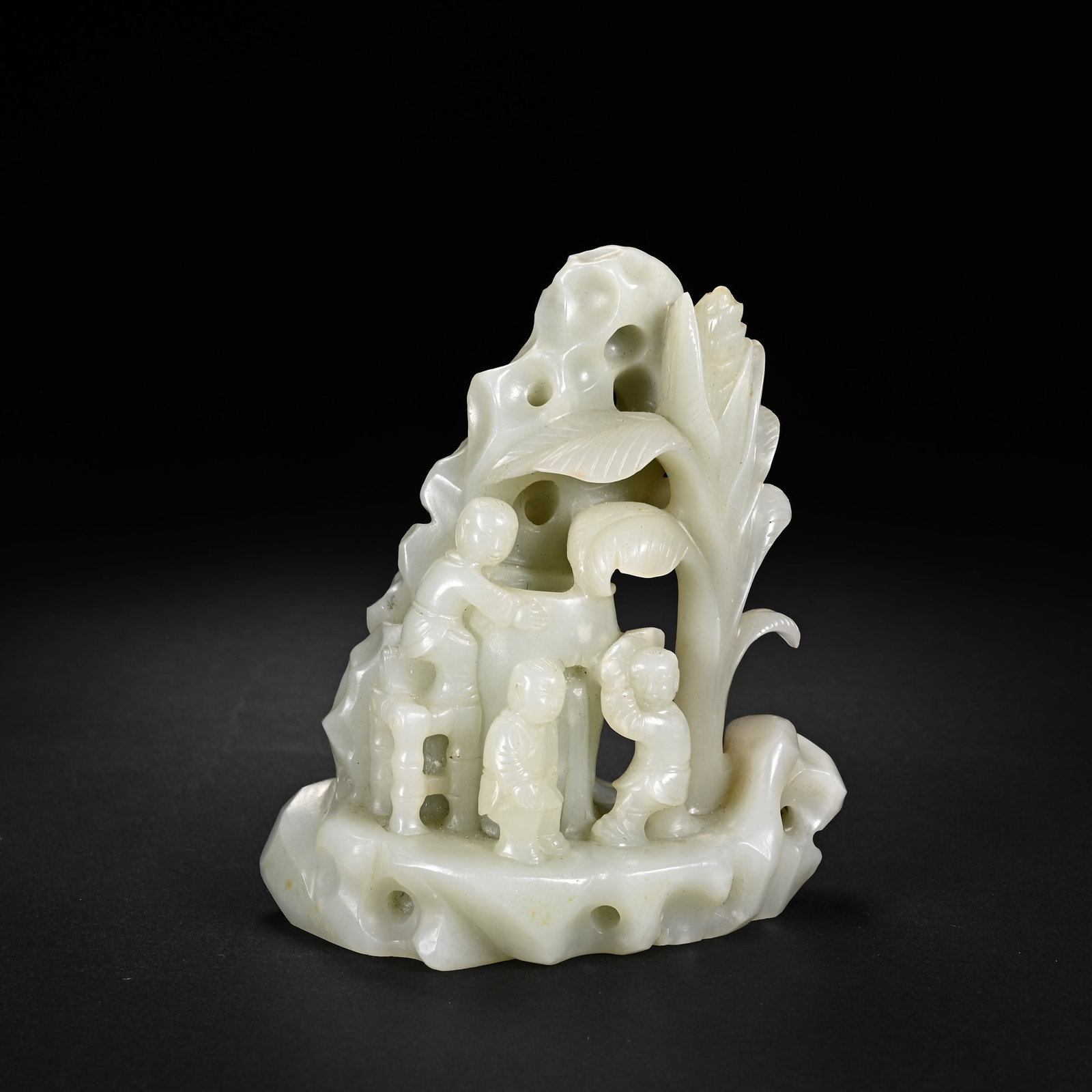 A CHINESE WHITE HETIAN JADE BOYS AT PLAY MOUNTAIN ORNAMENT: A CHINESE WHITE HETIAN JADE BOYS AT PLAY MOUNTAIN ORNAMENT This elaborate jade mountain carving is hollowed and sculpted from pale creamy Hetian nephrite with subtle faint russet flecks across its pol