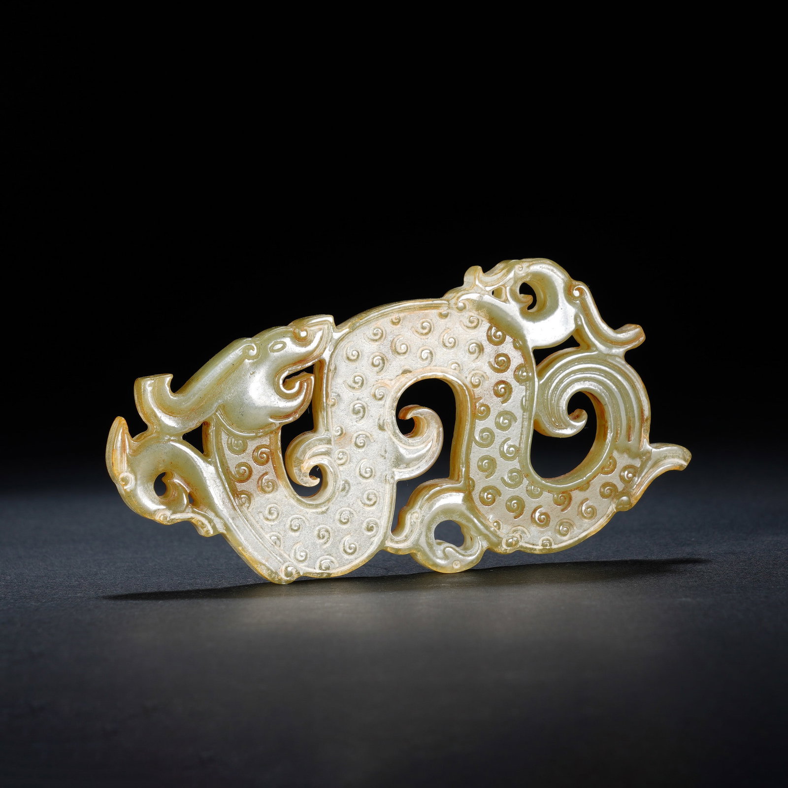 A CHINESE ARCHAIC JADE DRAGON PLAQUE: A CHINESE ARCHAIC JADE DRAGON PLAQUE This openwork jade dragon pendant measures 10 cm long, 5 cm wide and 0.6 cm thick, weighing 45 grams. Carved from pale celadon nephrite naturally suffused with war