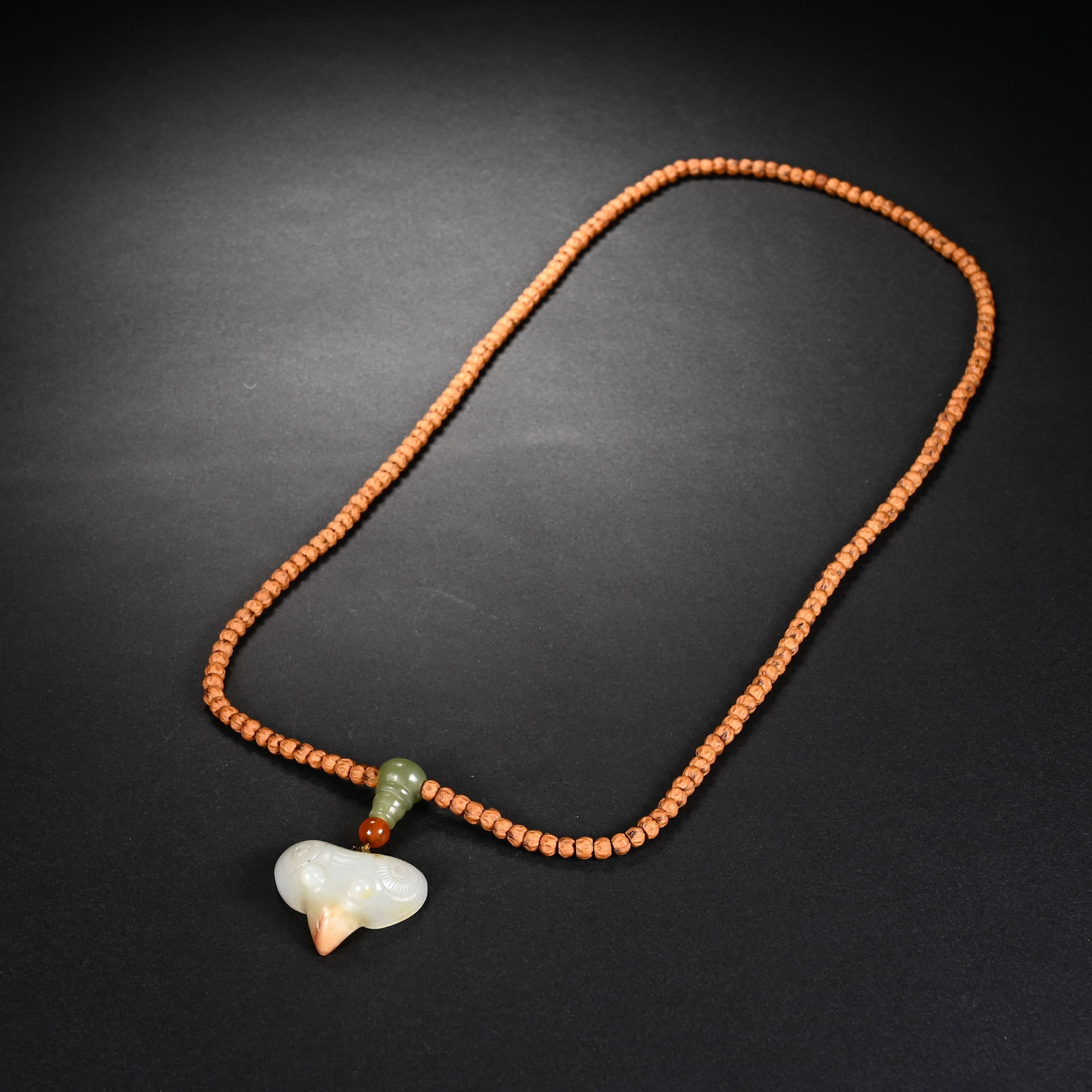 A CHINESE WHITE JADE BIRD HEAD PENDANT NECKLACE: A CHINESE WHITE JADE BIRD HEAD PENDANT NECKLACE This wearable strand is strung with uniform tiny rudraksha seed beads, matched with accent spacers of green jade gourd and small red agate bead. The foc