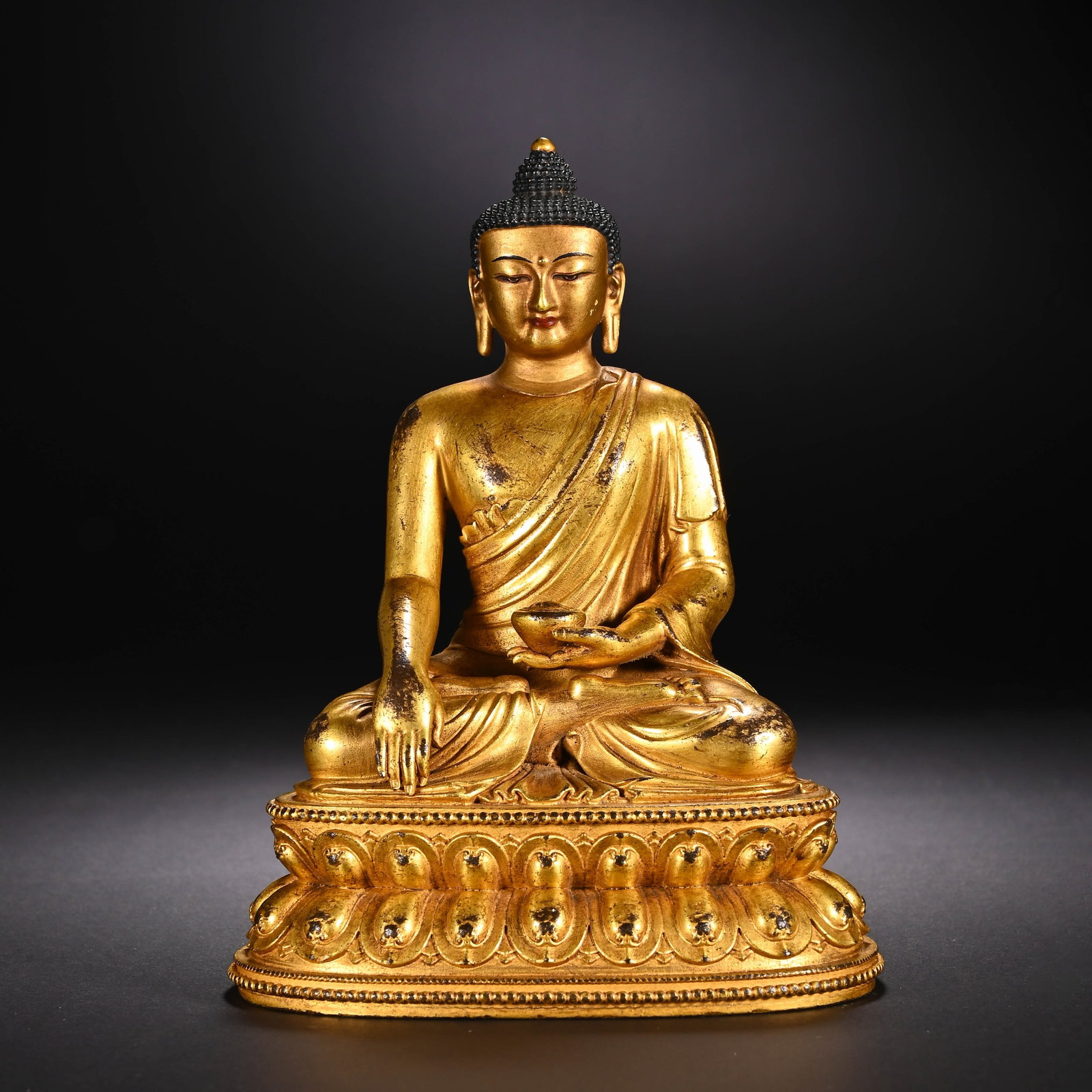 A CHINESE GILT BRONZE MEDICINE BUDDHA STATUE: A CHINESE GILT BRONZE MEDICINE BUDDHA STATUE This serene fully gilt bronze Medicine Buddha sits in full lotus position upon a double-tiered lotus pedestal bordered by delicate bead moulding. The Buddh