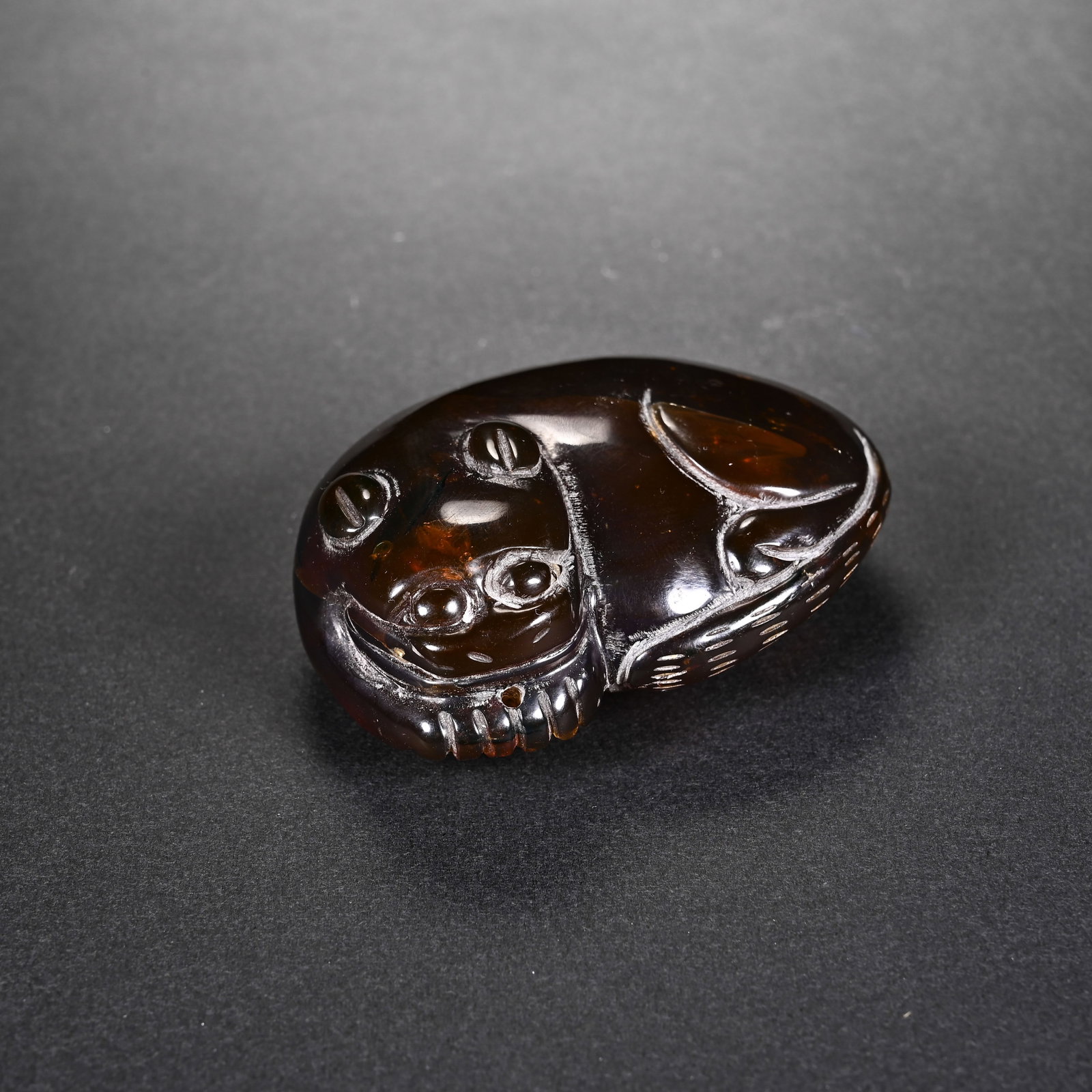 A CHINESE AMBER RECUMBENT MYTHICAL BEAST PENDANT: A CHINESE AMBER RECUMBENT MYTHICAL BEAST PENDANT This hand-carved ornament is crafted from translucent deep reddish-brown amber with a glossy polished surface, measuring 6.1cm long, 4.2cm wide and 2.3