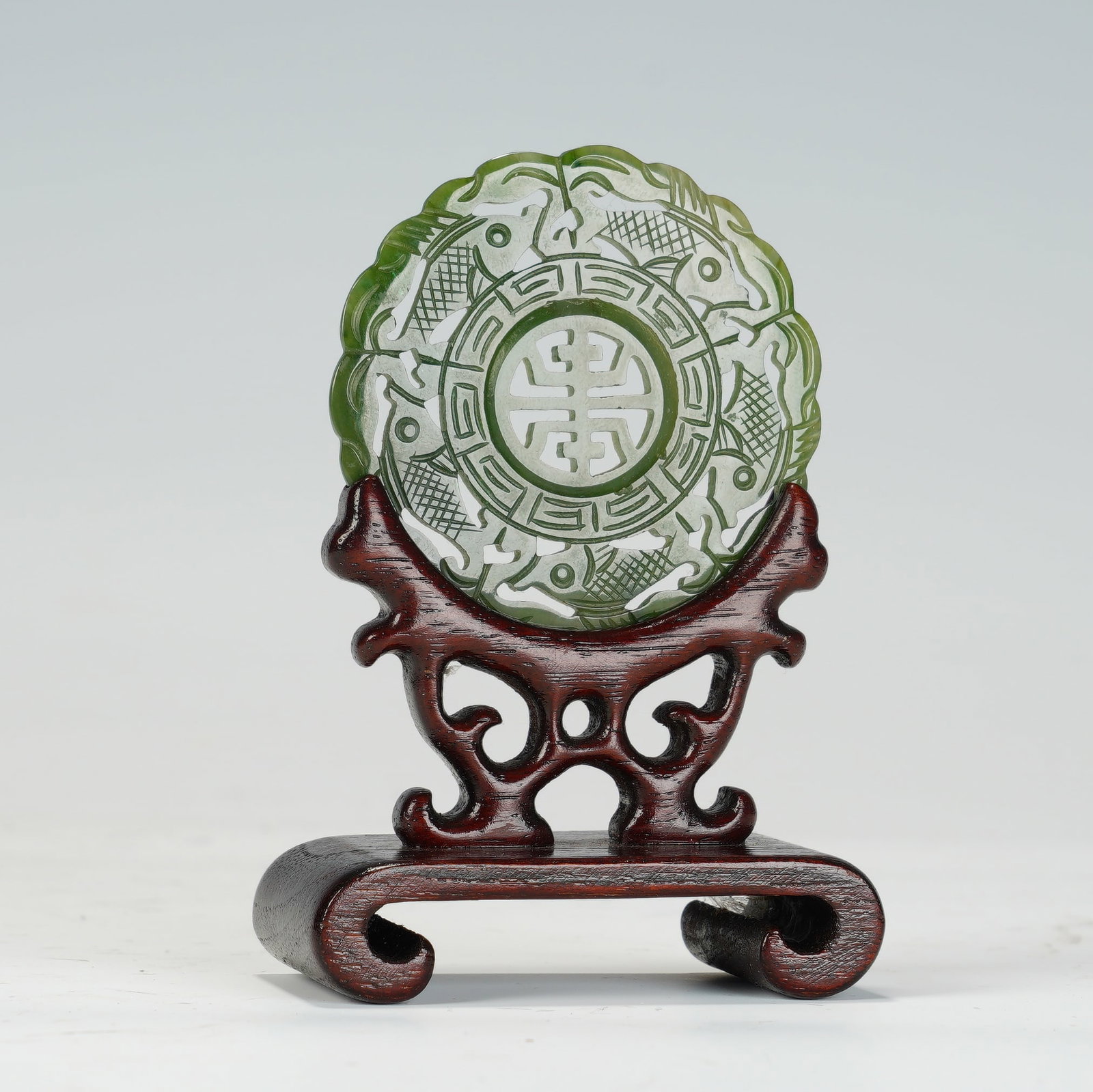 A CHINESE SPINACH JADE TABLE SCREEN WITH STAND: A CHINESE SPINACH JADE TABLE SCREEN WITH STAND The openwork spinach jade circular plaque measures 5.5 cm in diameter; the complete ensemble with carved hardwood stand is 6 cm wide, 3.5 cm deep and 9 c