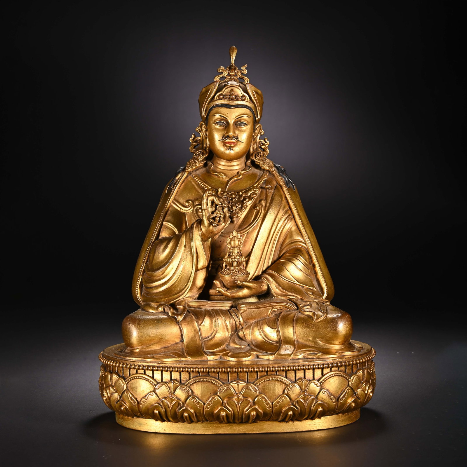 A CHINESE GILT BRONZE PADMASAMBHAVA STATUE: A CHINESE GILT BRONZE PADMASAMBHAVA STATUE This fully gilt bronze statue depicts Padmasambhava, known as Guru Rinpoche, seated in full lotus posture atop an ornate single lotus pedestal decorated with