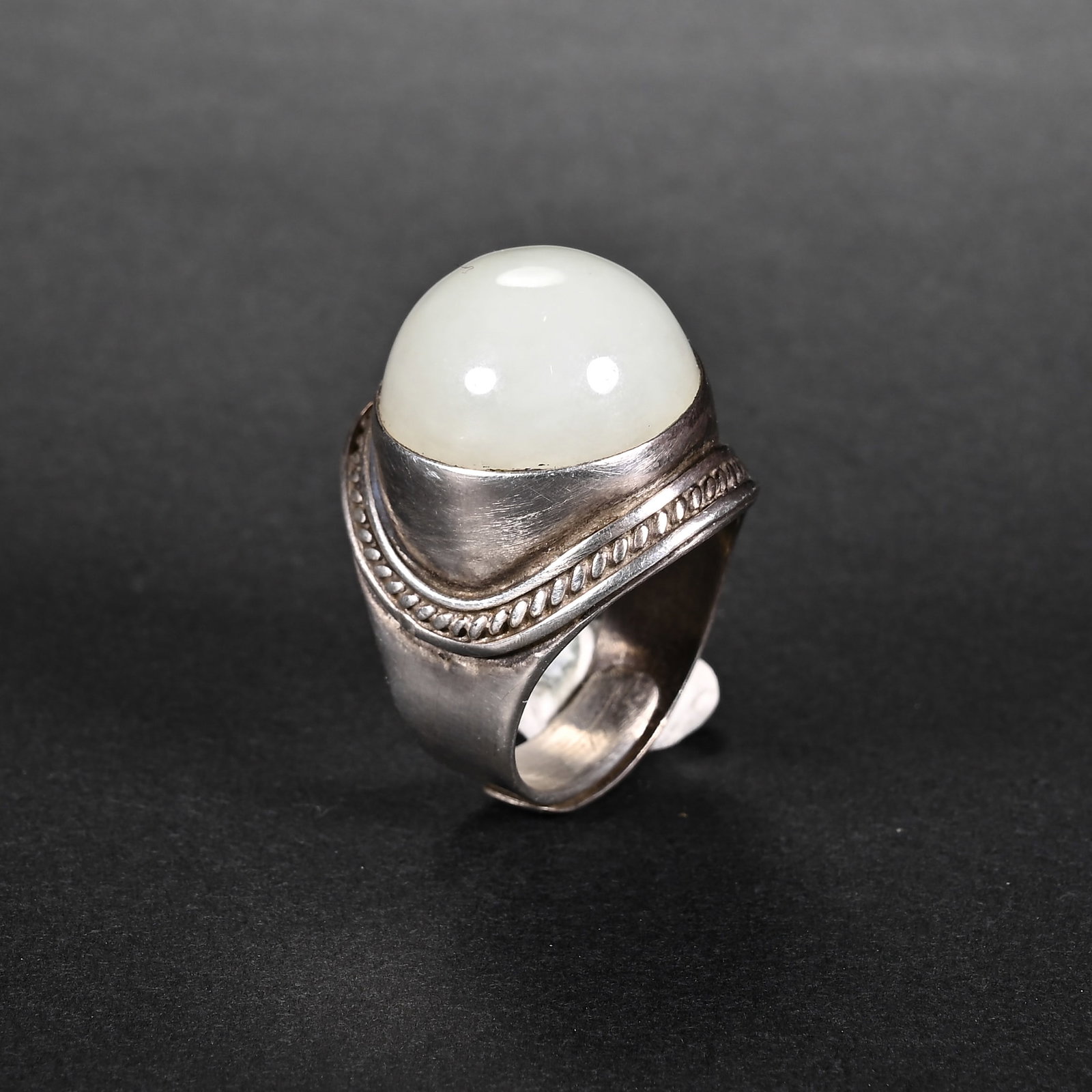 A CHINESE STERLING SILVER RING WITH WHITE JADE CABOCHON: A CHINESE STERLING SILVER RING WITH WHITE JADE CABOCHON This vintage signet-style ring features a large smooth oval cabochon of pale white Hetian nephrite as its central stone, measuring 2cm by 2.2cm.