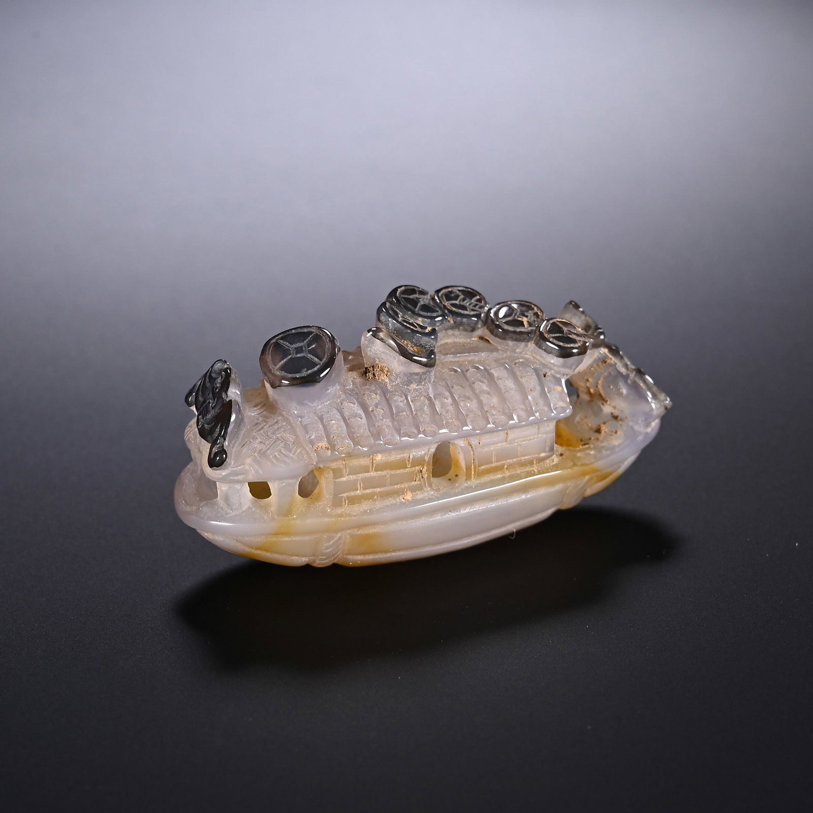 A CHINESE CAMEO AGATE WEALTH BOAT PENDANT TOGGLE: A CHINESE CAMEO AGATE WEALTH BOAT PENDANT TOGGLE This miniature hand-carved pendant is crafted from natural translucent agate with warm amber base hues and distinctive dark grey natural inclusions ski