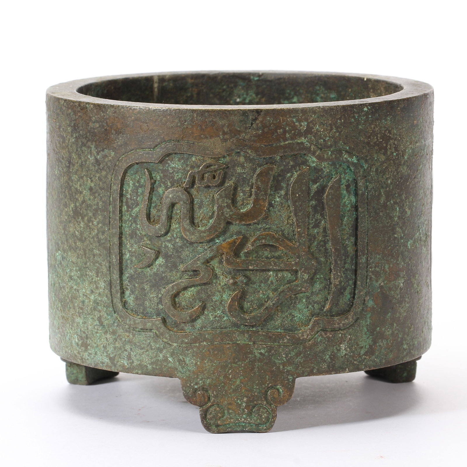 A CHINESE ARABIC CALLIGRAPHY TRIPOD BRONZE CENSER: A CHINESE ARABIC CALLIGRAPHY TRIPOD BRONZE CENSER This cylindrical bronze censer stands on three stylized ruyi-shaped feet and is blanketed in thick natural verdigris patina across both interior and e