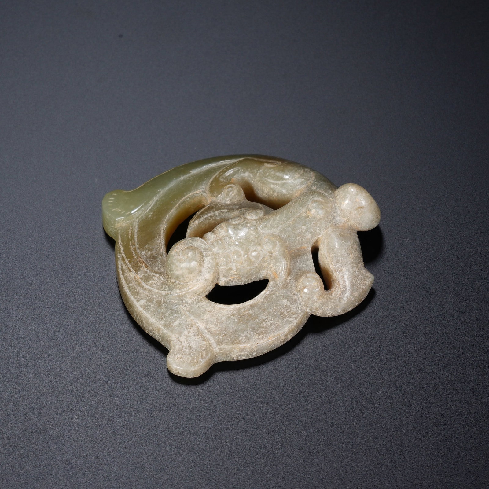A CHINESE ARCHAIC JADE CHILONG PENDANT: A CHINESE ARCHAIC JADE CHILONG PENDANT This openwork jade chilong ornament measures 5.4 cm long, 4.7 cm wide and 1.6 cm thick, weighing 37 grams. Carved from celadon nephrite partially covered in pale