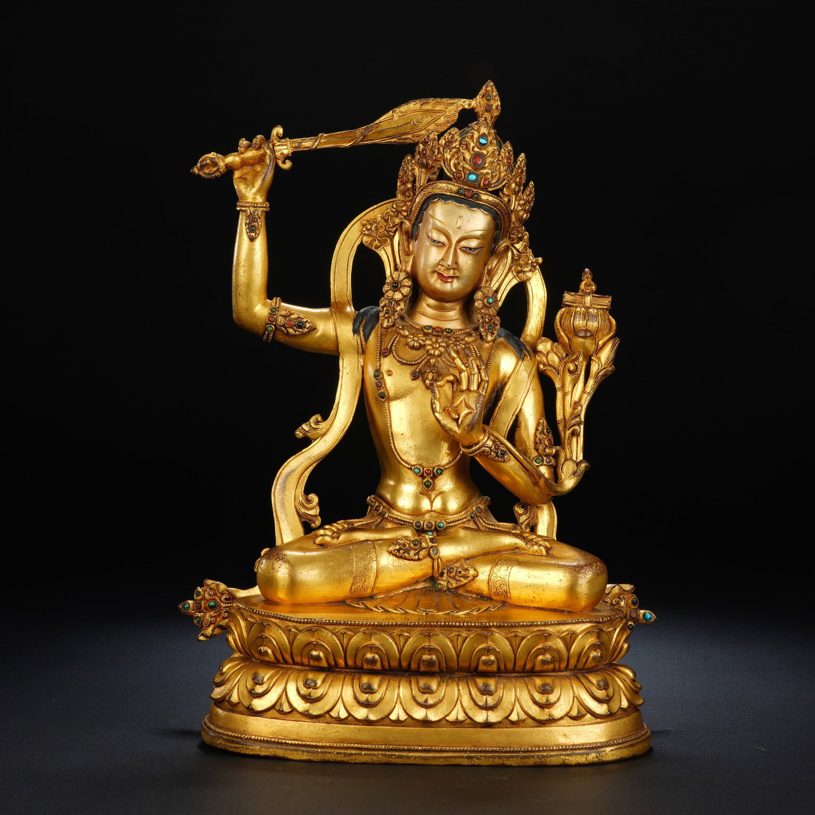 A CHINESE JEWELLED GILT BRONZE SEATED MANJUSHRI: A CHINESE JEWELLED GILT BRONZE SEATED MANJUSHRI This cast gilt bronze Manjushri statue measures 17cm ? 11cm ? 26cm and weighs 2979 grams. The Bodhisattva sits in full lotus meditation pose upon a two-