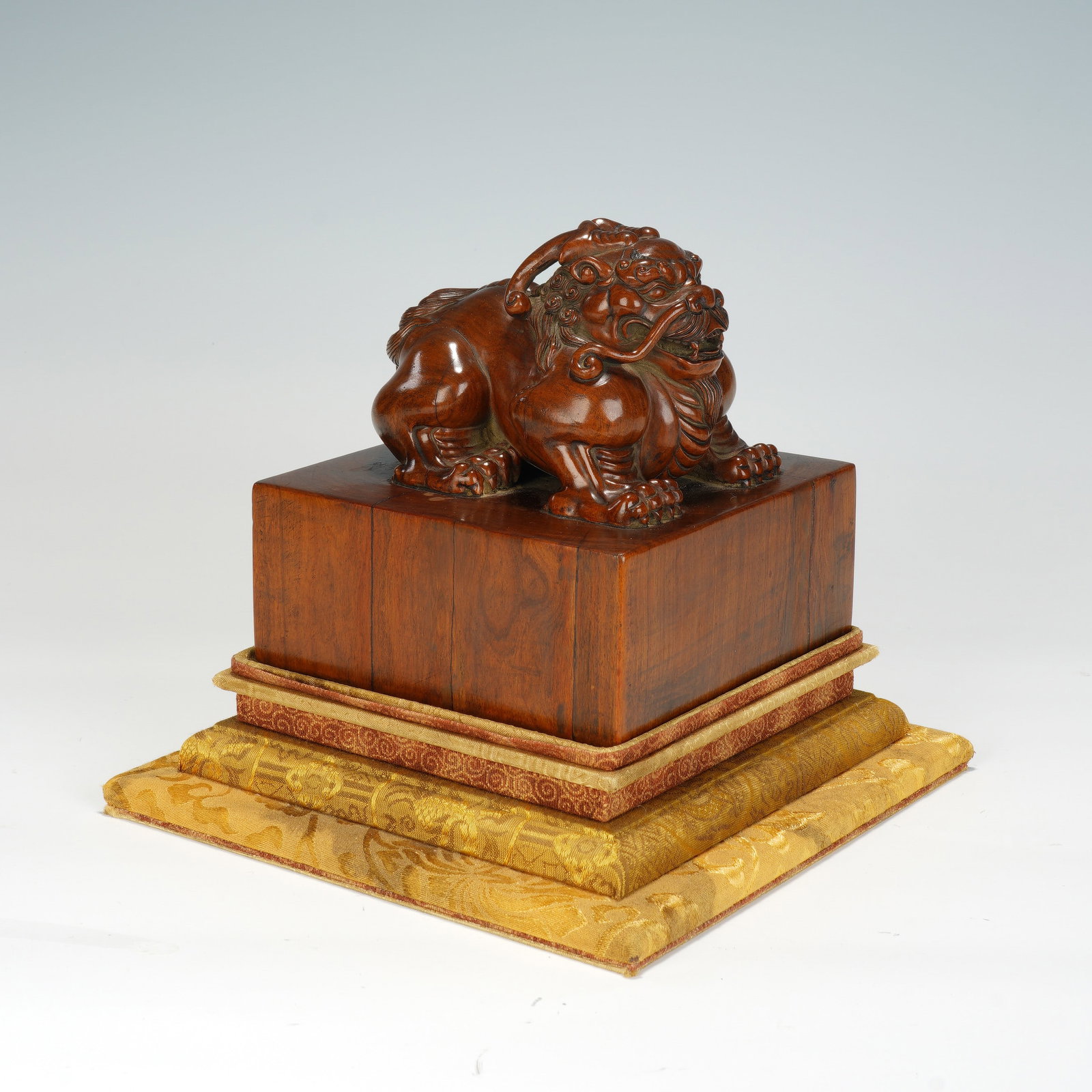 A CHINESE BOXWOOD LION FINIAL SEAL: A CHINESE BOXWOOD LION FINIAL SEAL This solid square boxwood seal block measures 14.5 cm on each side, with an overall height of 19 cm. The top is surmounted by a fully carved recumbent guardian lion 