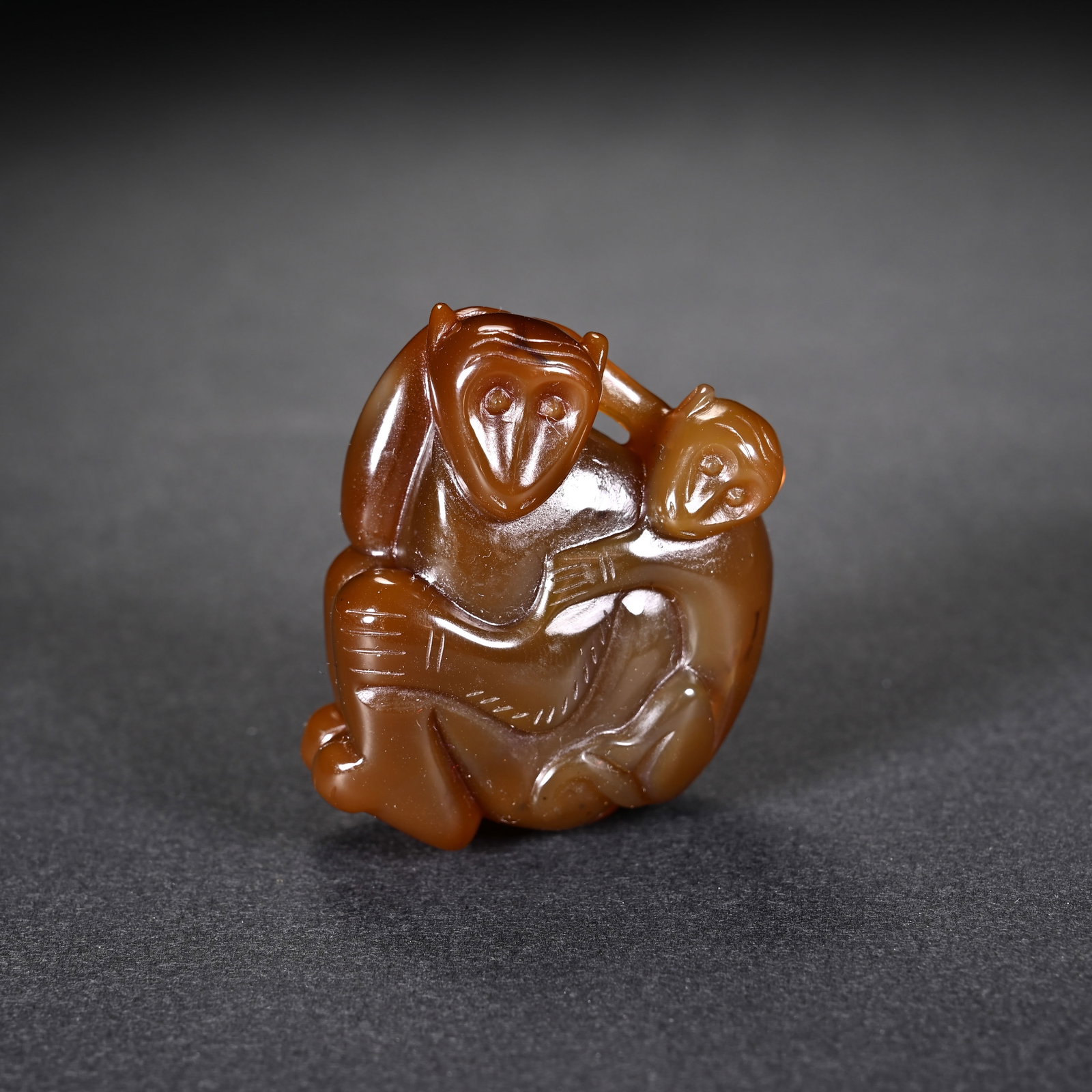 A CHINESE AGATE MOTHER AND INFANT MONKEY PENDANT: A CHINESE AGATE MOTHER AND INFANT MONKEY PENDANT This wearable carving is fashioned from warm translucent caramel agate with smooth glossy polish and unified earthy amber tones. It depicts a seated ad