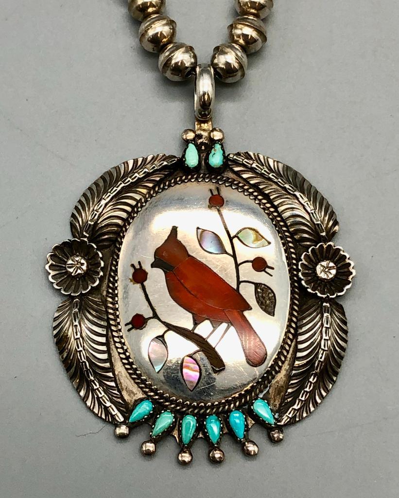 Sterling Silver Turquoise and Inlay Necklace- Stanley Gene: Available in this lot is a sterling silver, turquoise and inlay necklace by Stanley Gene. This exquisite necklace features an inlay of coral, onyx, and mother of pearl set in a bird (cardinal) design.