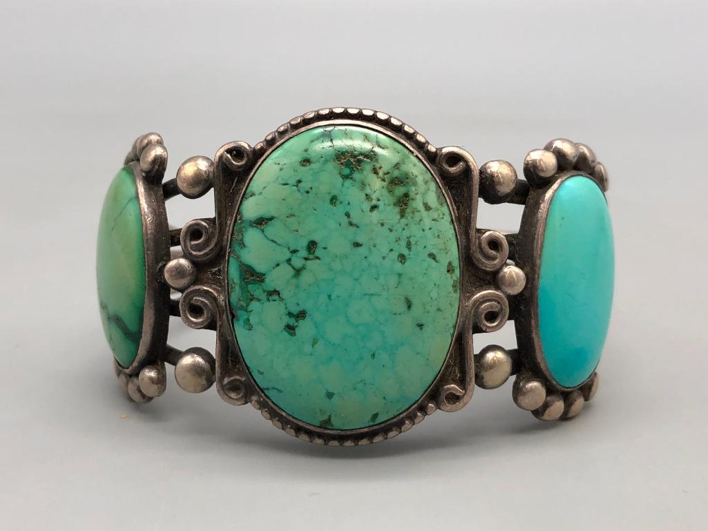 Vintage Three Stone Turquoise Bracelet: Offered in this lot is a vintage three stone turquoise bracelet. The stones on this bracelet are large green hued turquoise, surrounded by silverwork of dots, and loops of wire. The sterling silver ba