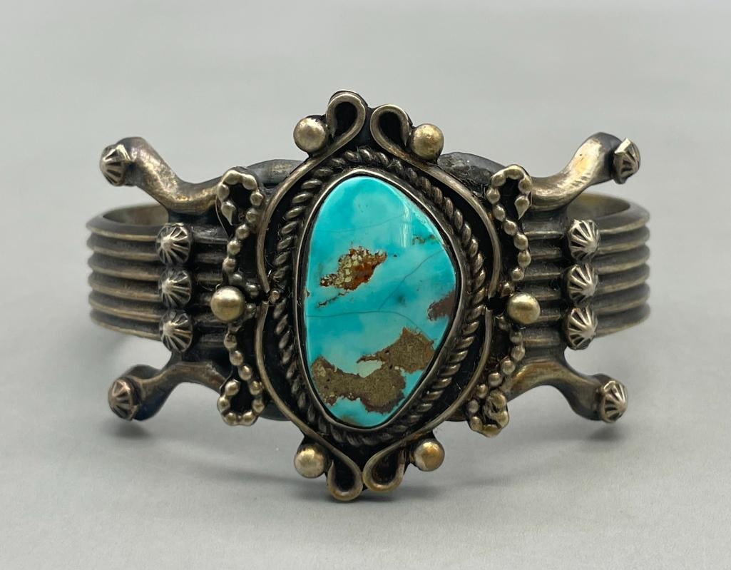Turquoise And Sterling Silver Bracelet By F. L. Begay: For your bidding enjoyment we present a turquoise and sterling silver bracelet by F. L. Begay. This bracelet features a central turquoise cabochon displayed in a smooth silver bezel. Surrounding the s