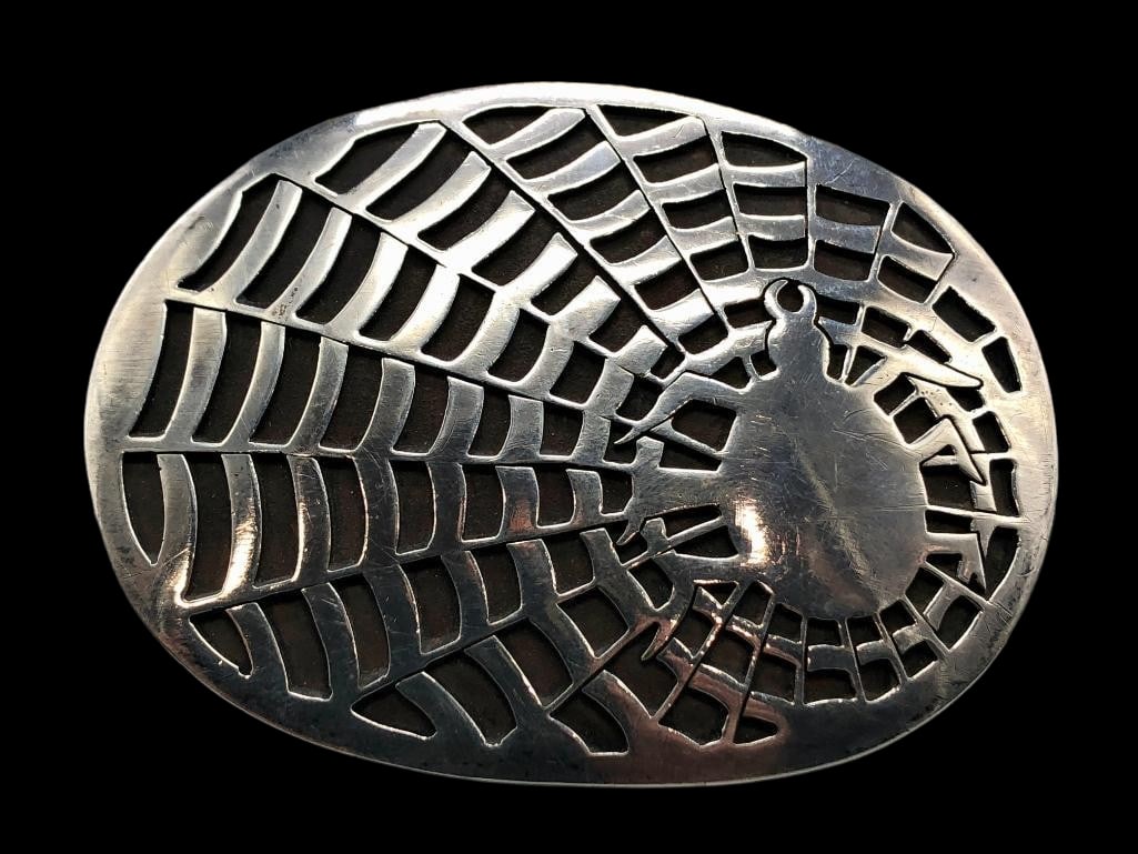 Spiderweb Sterling Silver Belt Buckle: Available here in this lot is a spiderweb sterling silver belt buckle. This sterling silver belt buckle features a striking spider in a web overlay design set against a darkened silver background that