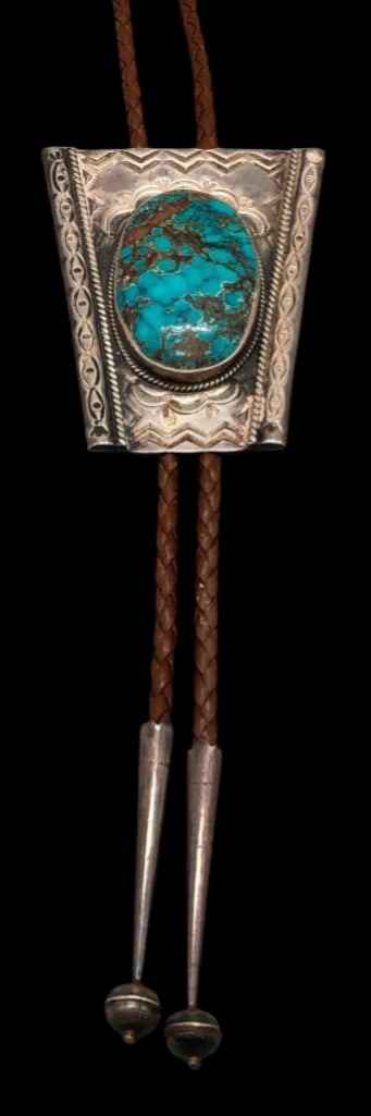 Nice Turquoise Bolo Tie by Dean Sandoval Jr.: Offered in this lot is a nice turquoise bolo tie by Dean Sandoval, Jr. This slide features a beautiful turquoise cabochon resting in a smooth silver bezel surrounded by twisted wire and hand stamped d
