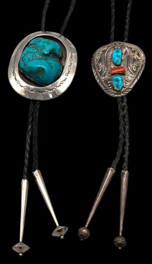 Two Signed Turquoise Bolo Ties: Offered in this lot are two signed turquoise bolo ties. One features a large nugget style turquoise cabochon resting in a smooth silver bezel on an oval silver setting highlighted with a shadow box de