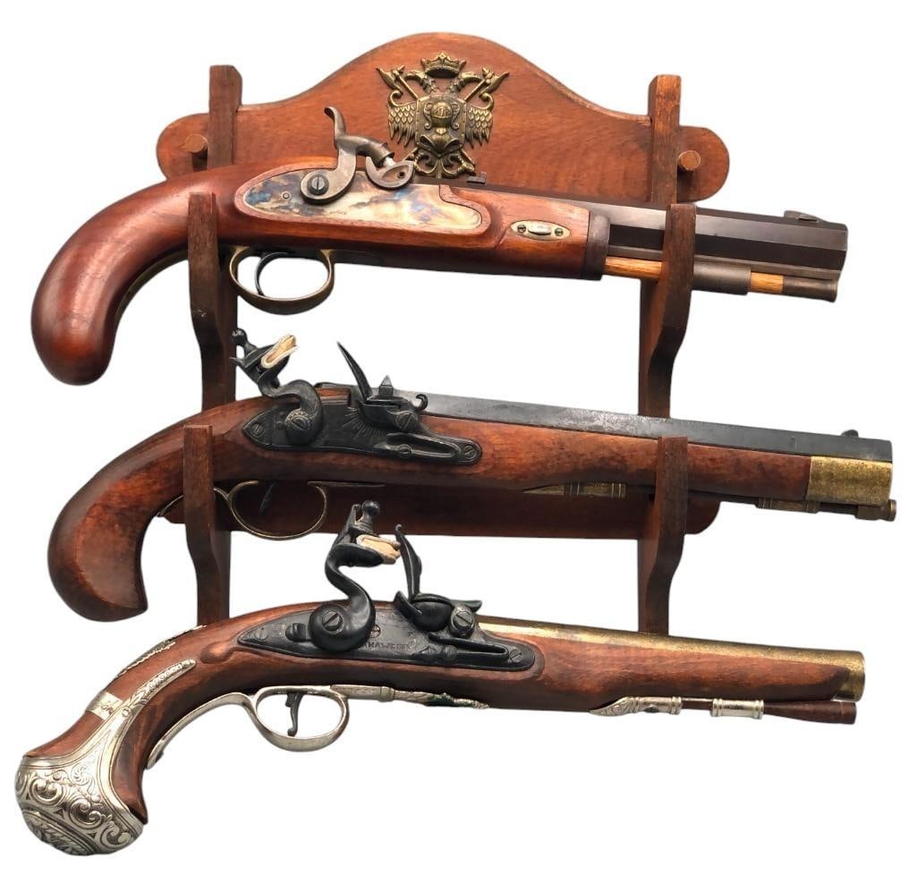 Three Black Powder Reproduction Pistols With Display Rack: Offered here for your consideration is a group of three black powder pistols style with a wooden display rack (for 2 of them). Included are 2 flintlock (non-firing) replicas and 1 percussion style (fi