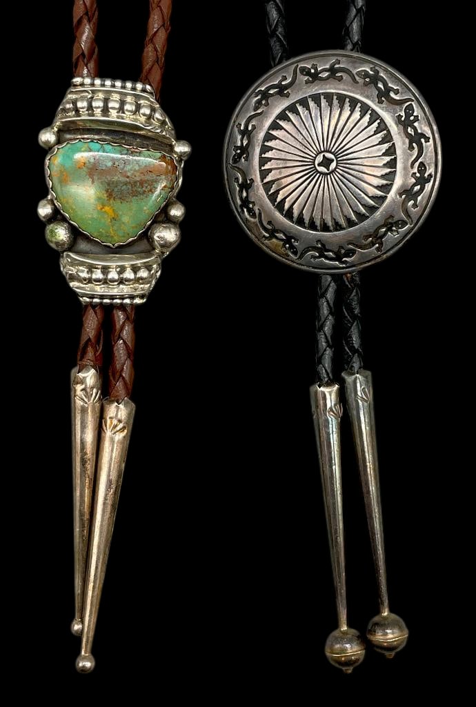 Two Sterling Silver Bolo Ties: Available here in this lot are two sterling silver bolo ties. One bolo features a round concho style silver slide with radiating stamped patterns. The other features a turquoise cabochon set in a