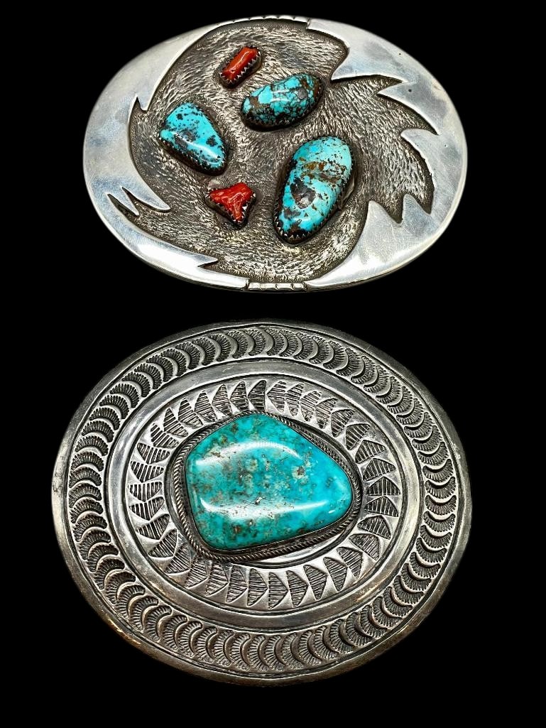 Two Sterling Silver And Turquoise Belt Buckles - One with Coral: Available here in this lot are two sterling silver and turquoise belt buckles- one with coral. Both pieces feature turquoise cabochons with one further highlighted with two coral cabochons. The