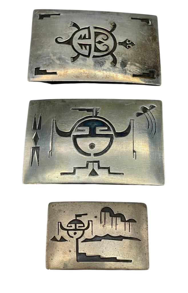 Three Sterling Silver Buckles By Willie Yazzie Sr.: Offered here in this lot are three sterling silver buckles by Willie Yazzie Sr.. These items feature overlay designs of a Horned Moon with clouds or a turtle. Accenting them are darkened backgrounds w