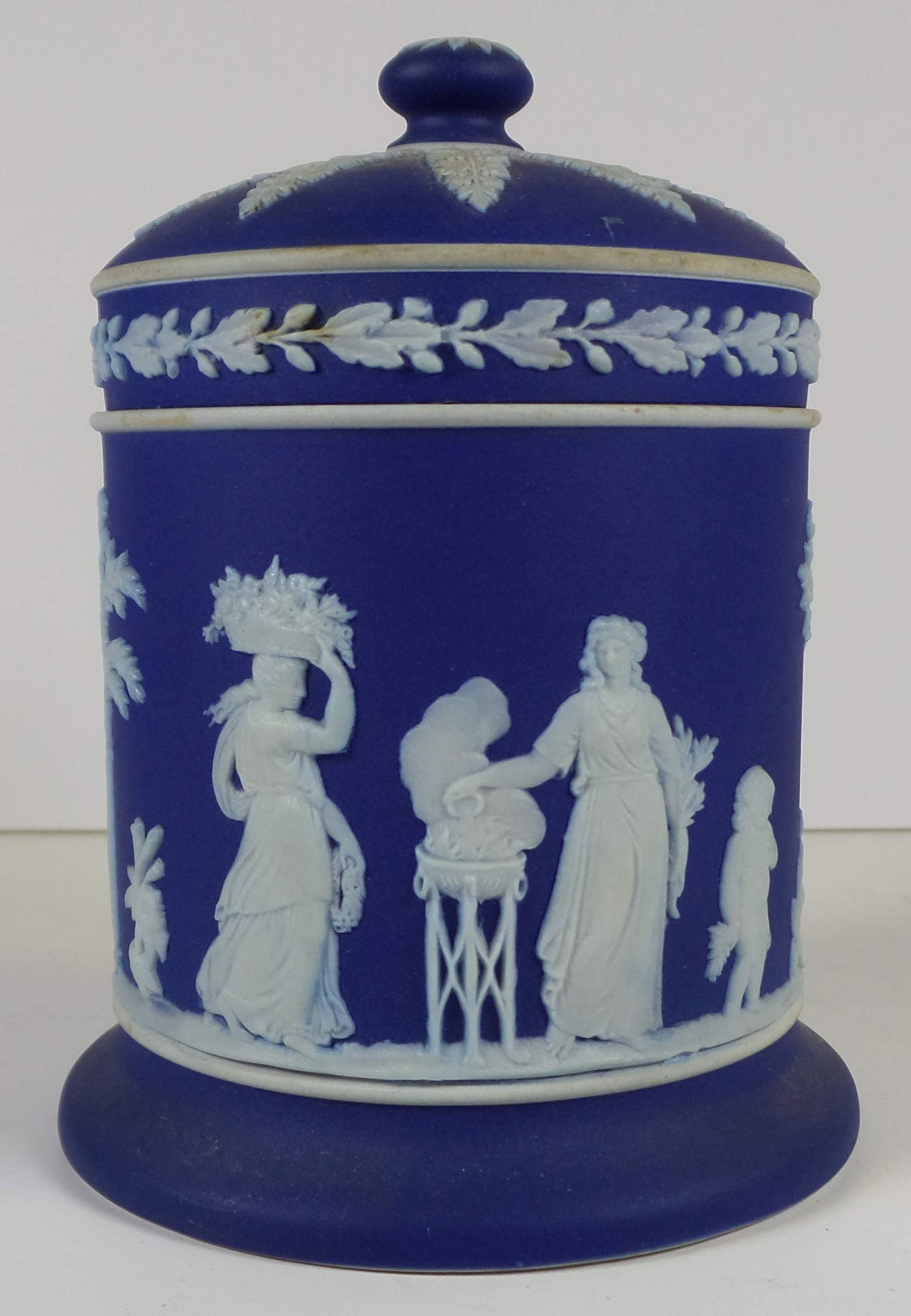 Vintage WEDGWOOD Jasperware Dark Blue Neoclassical Tobacco Jar: A beautiful deep blue Wedgwood tobacco jar with raised neoclassical motif and scrolling floral design to lid. Marked "Wedgwood Made in England." Measures approx. 5" x 3" x 3". Provenance: From the col